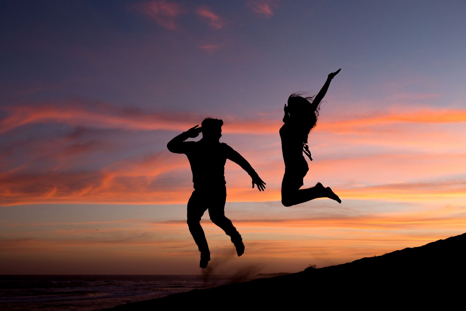 Silhouettes of two people jumping joyfully against a vibrant orange and purple sunset sky.