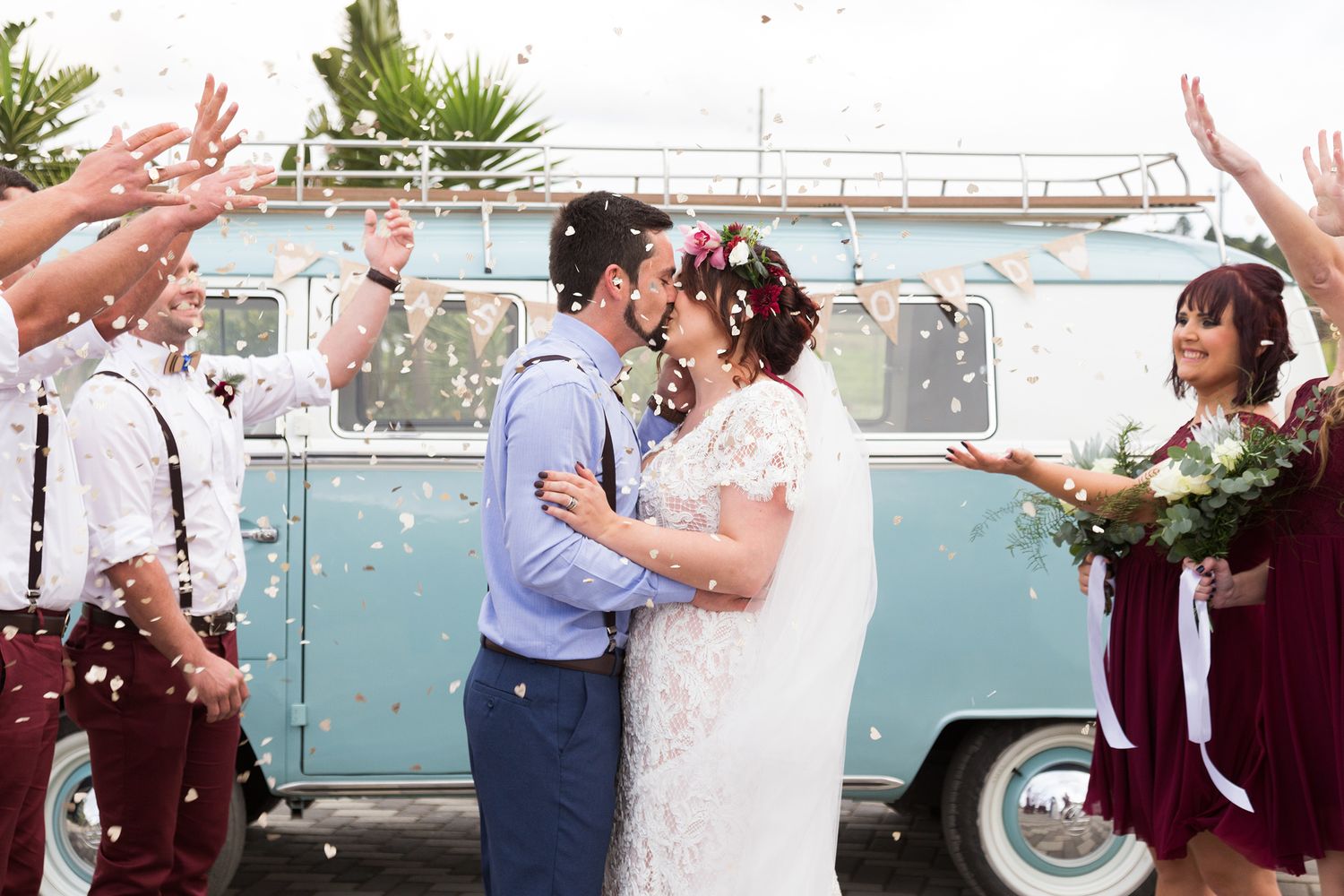 Wedding guests shower newlyweds with flower petals during a festive outdoor celebration at a scenic venue.