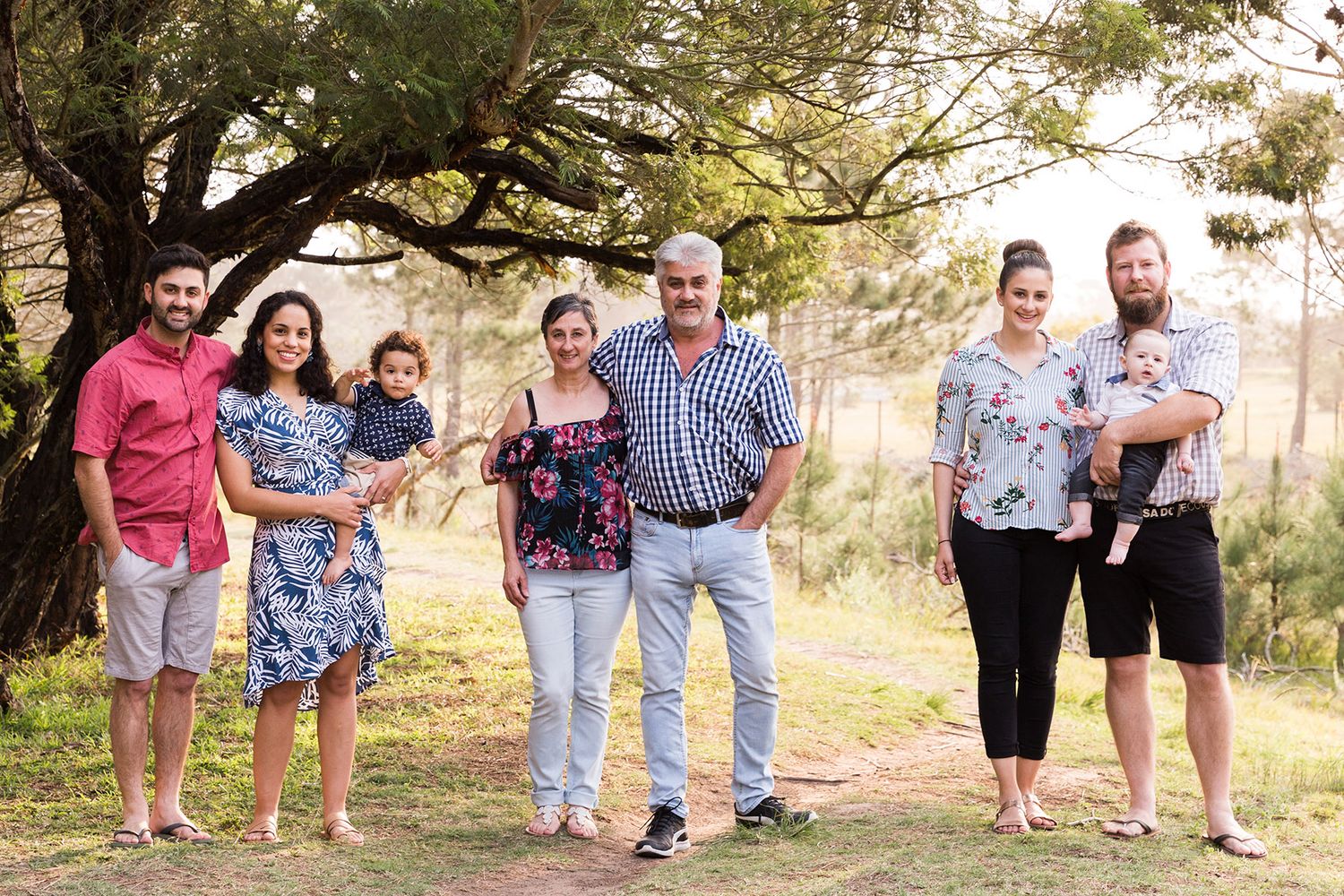Family members smiling while posing together outdoors in a natural setting with trees in the background.