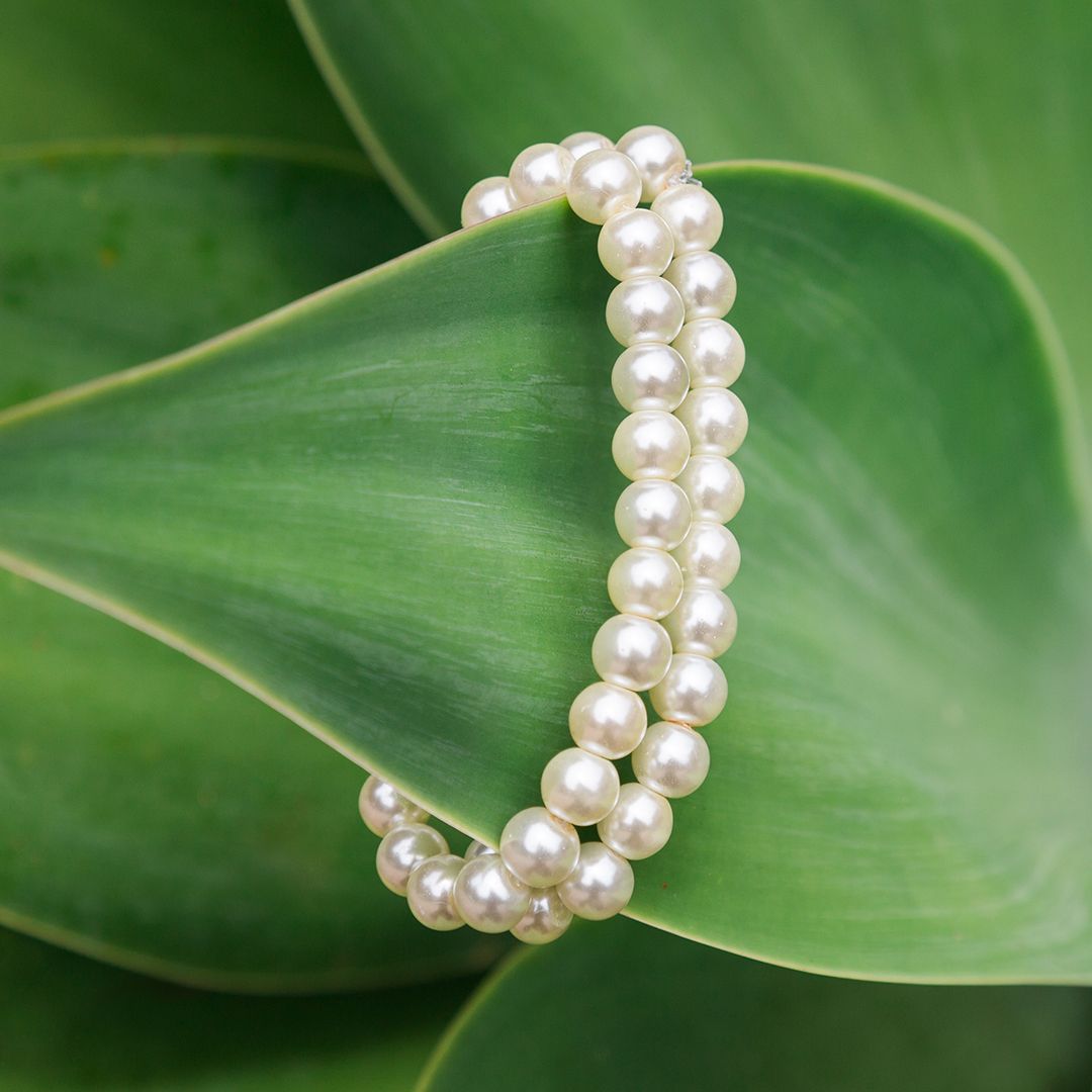 Sleek typography design formed with delicate white pearls against a vibrant green leaf background.