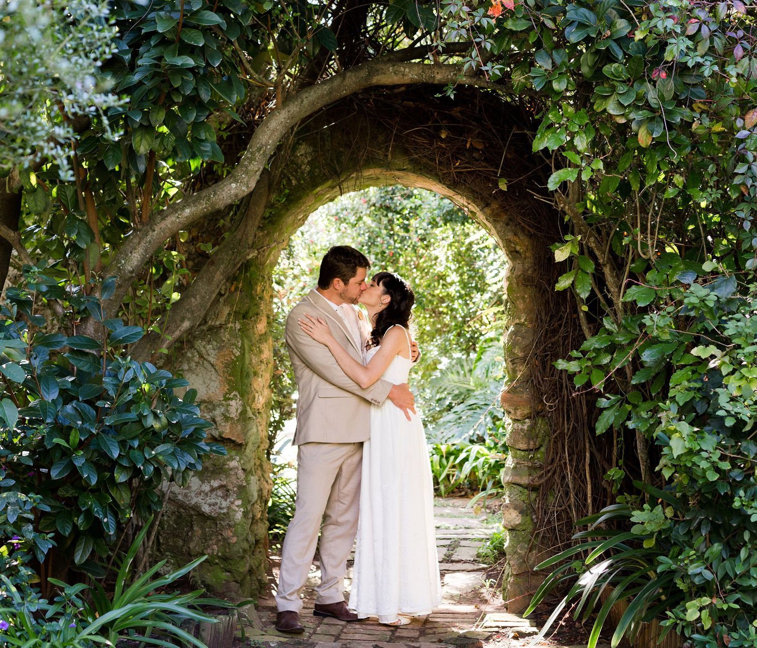 A romantic couple embraces under a lush green garden archway in a series of tender wedding photos.