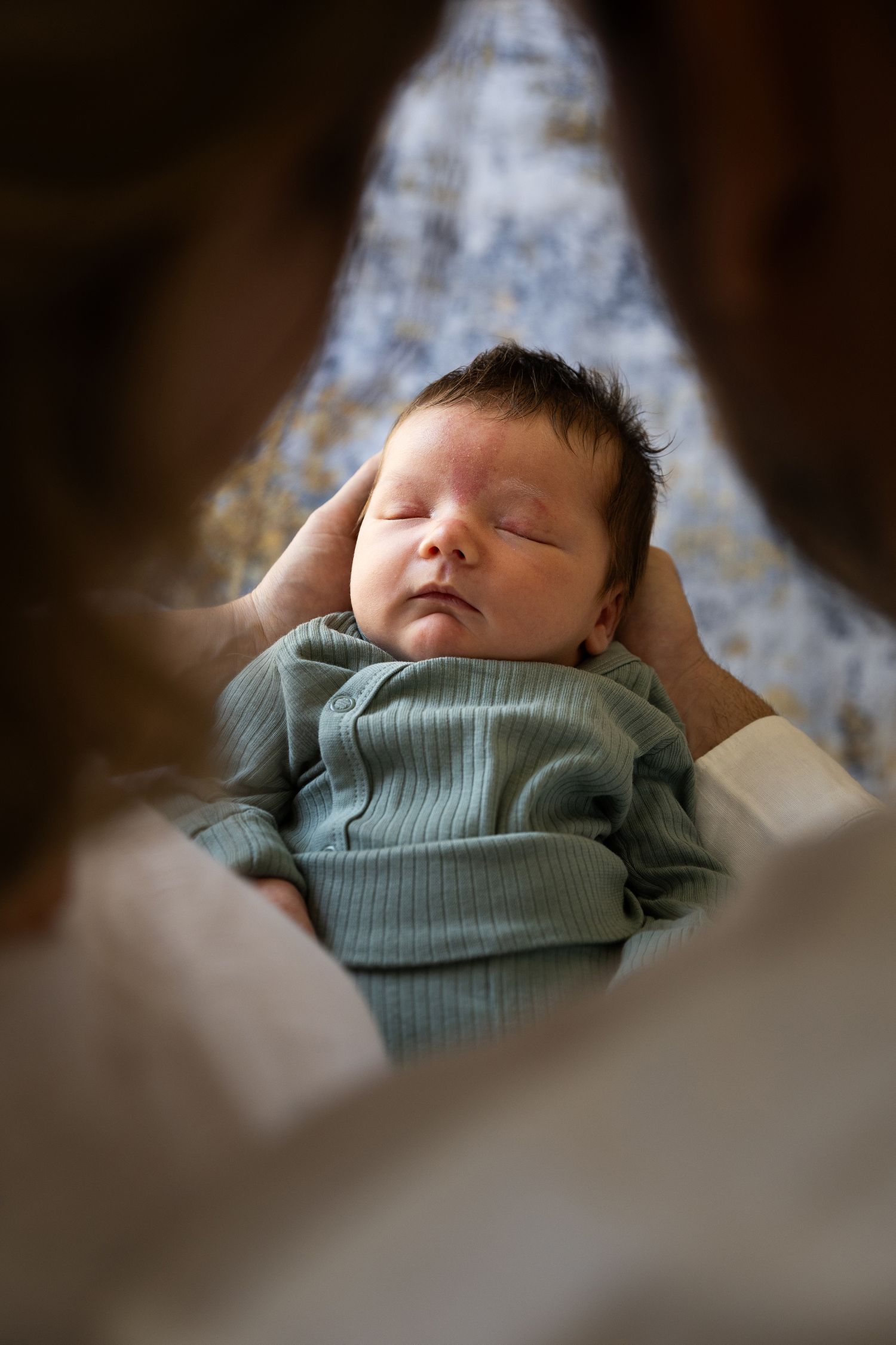 A sleeping baby wearing a mint green sweater nestles peacefully in soft white bedding while taking a daytime nap.
