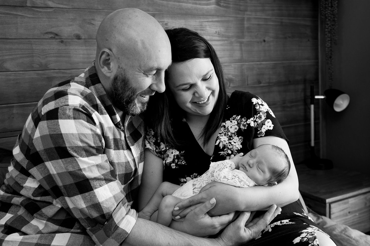 A heartwarming black and white portrait of loving parents gazing adoringly at their newborn baby.