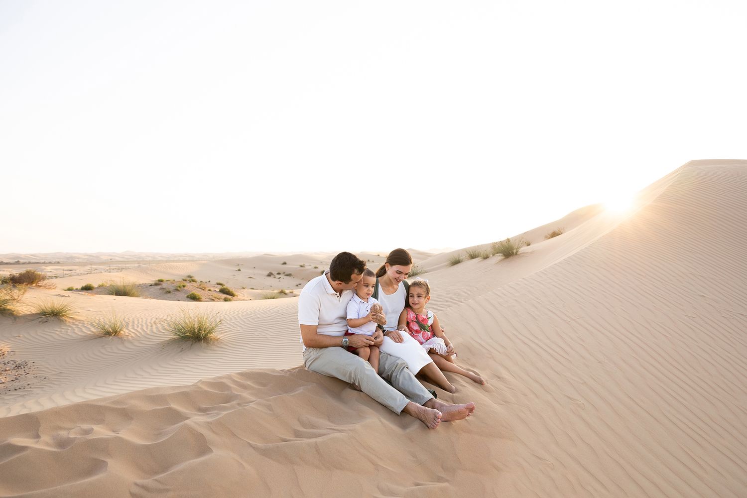 Couple lying on sandy dunes during sunset in desert landscape with multiple frames showing romantic poses.