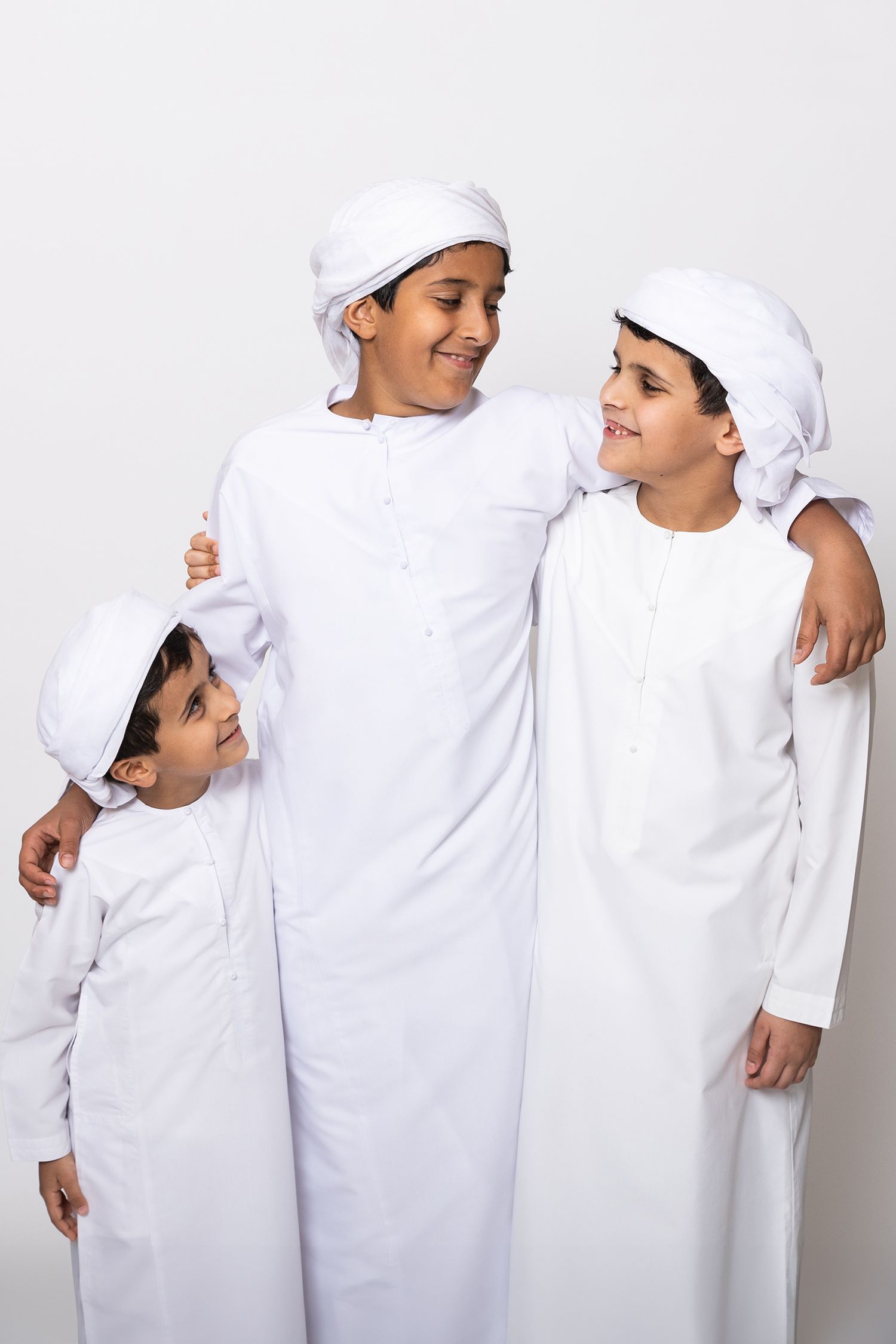 Three young boys in traditional white Middle Eastern dress and head coverings share a joyful moment together.