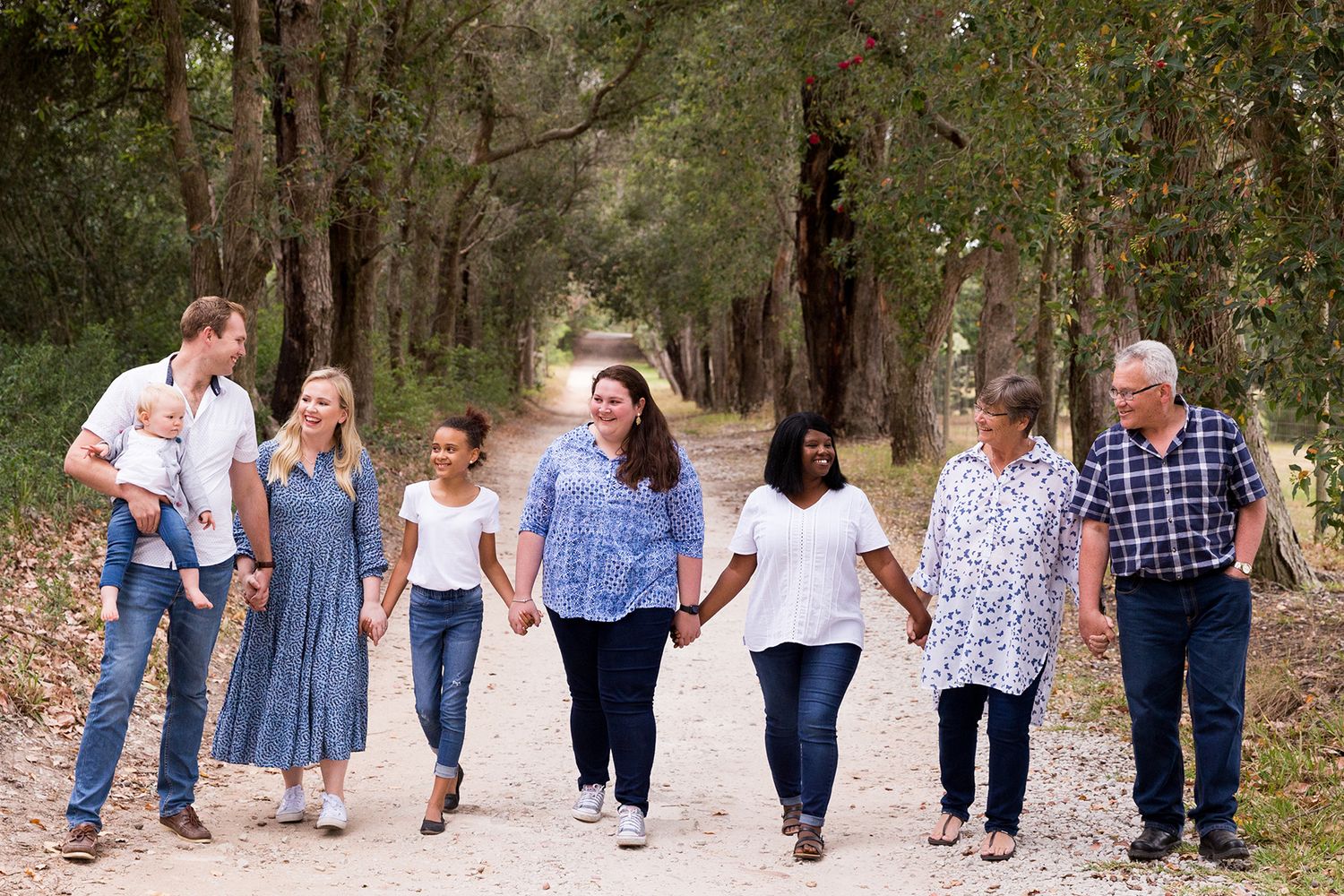 Group of people walking together on a winding dirt path through a wooded area wearing casual clothing and jeans.