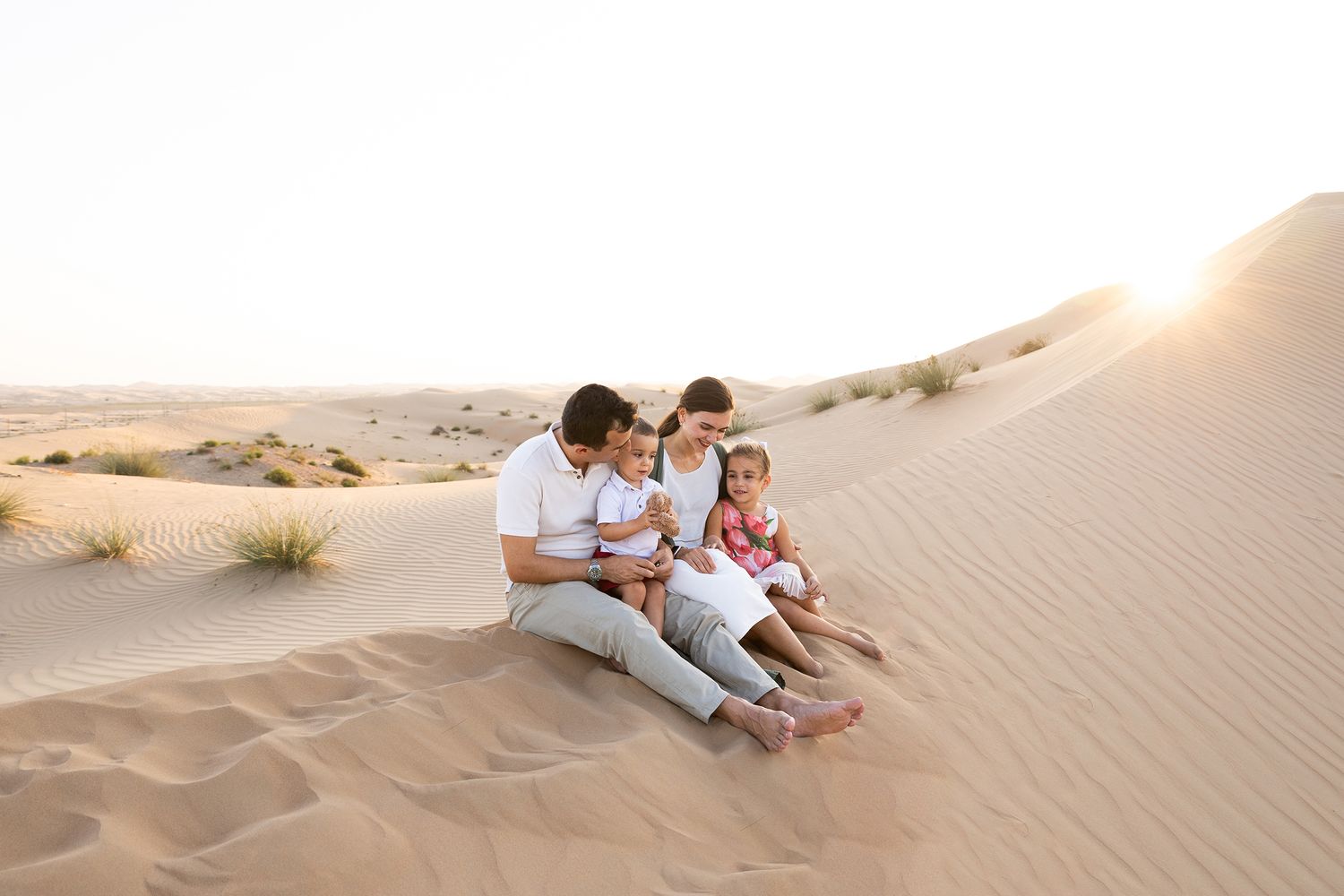 Couple sitting on golden sand dunes during sunset in a desert landscape.