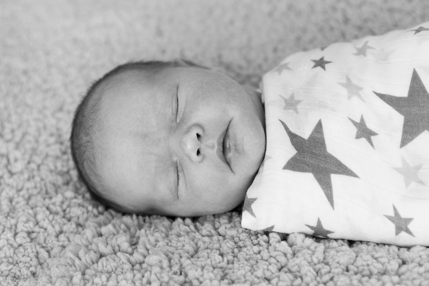 A black and white collage of newborn baby photos with star-patterned swaddle blanket.