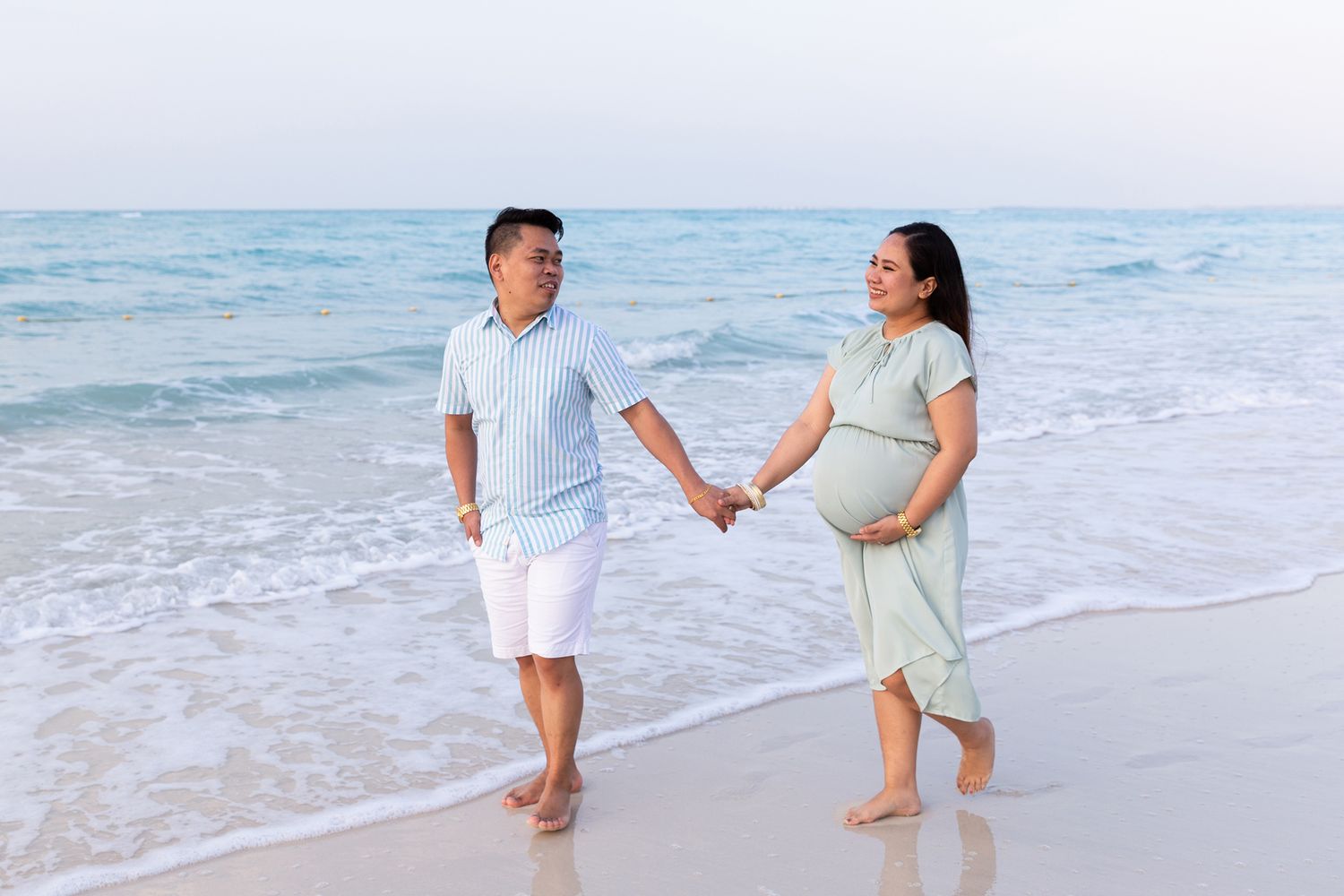 A couple in white clothing poses on a sandy beach at sunset creating a romantic ambiance by the ocean.