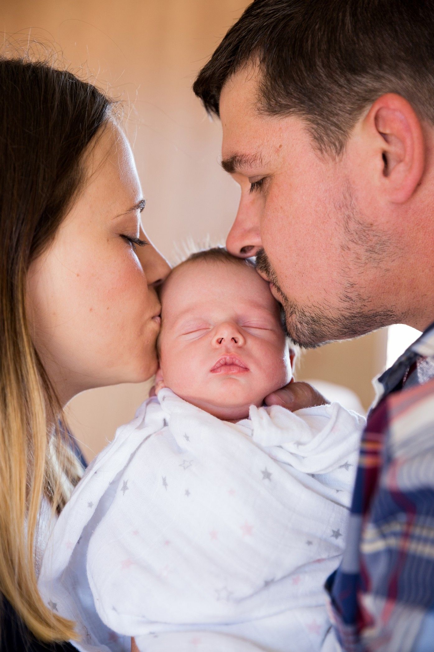 Parents sharing loving kisses with their newborn baby dressed in white in a touching sequence of photos.