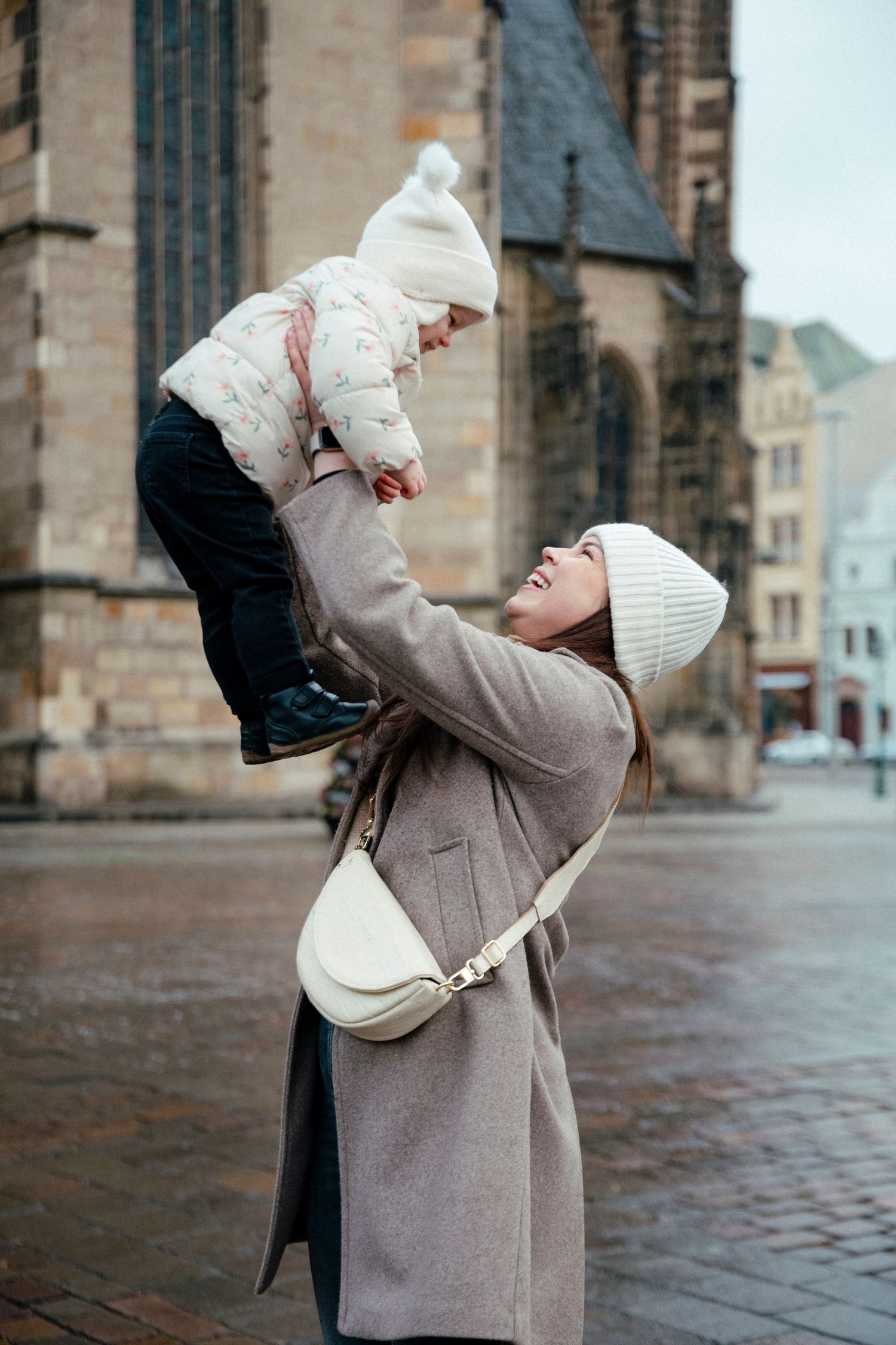 Parent lifting child playfully in front of historic architecture on rainy day.