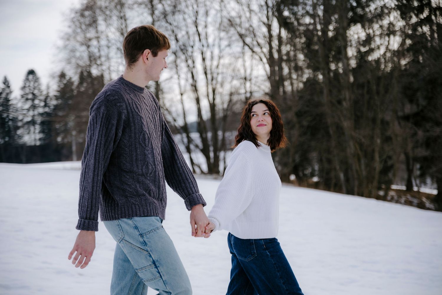 Couple walking together in snowy winter landscape with bare trees.