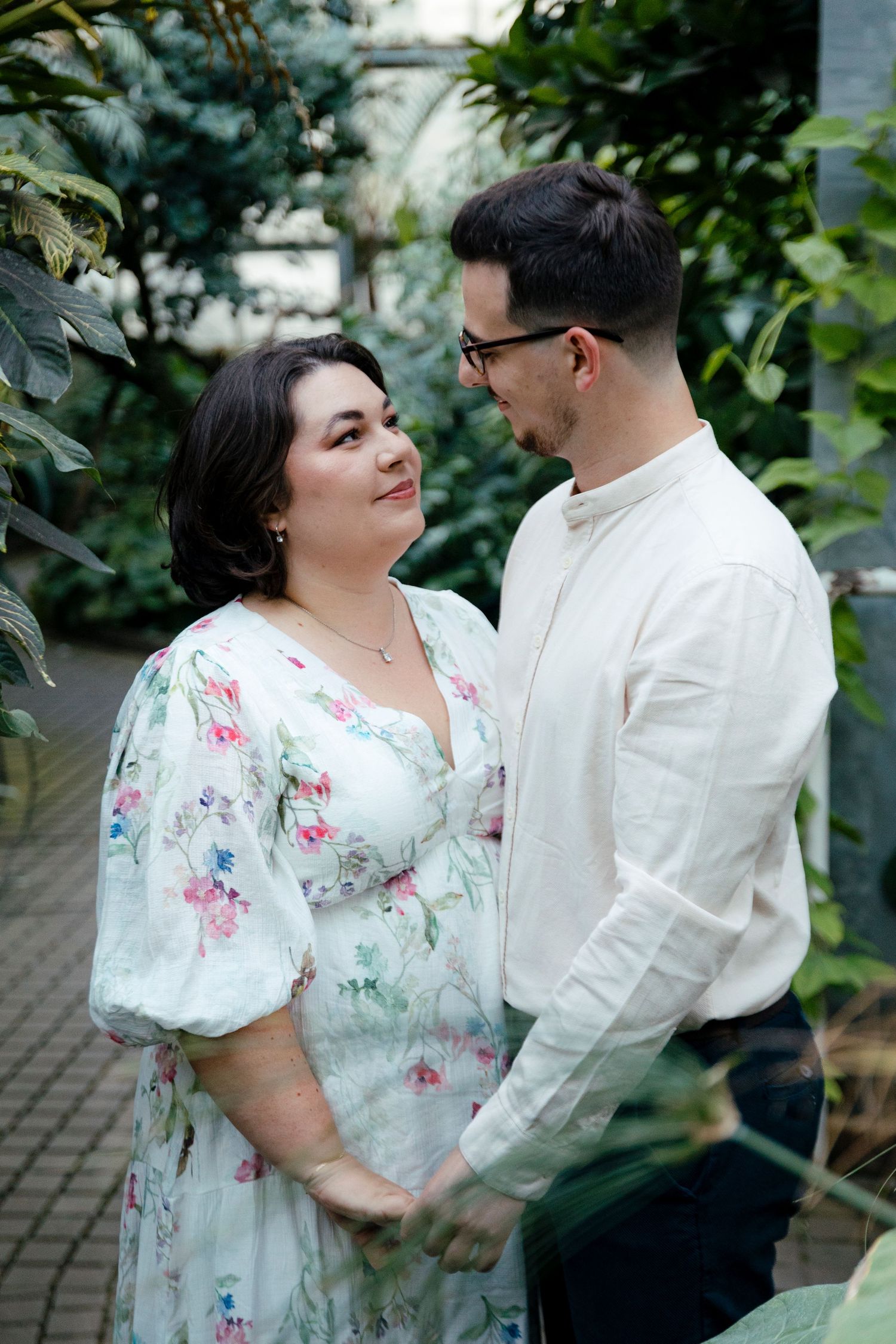 Romantic couple poses in garden setting wearing white and floral clothing.