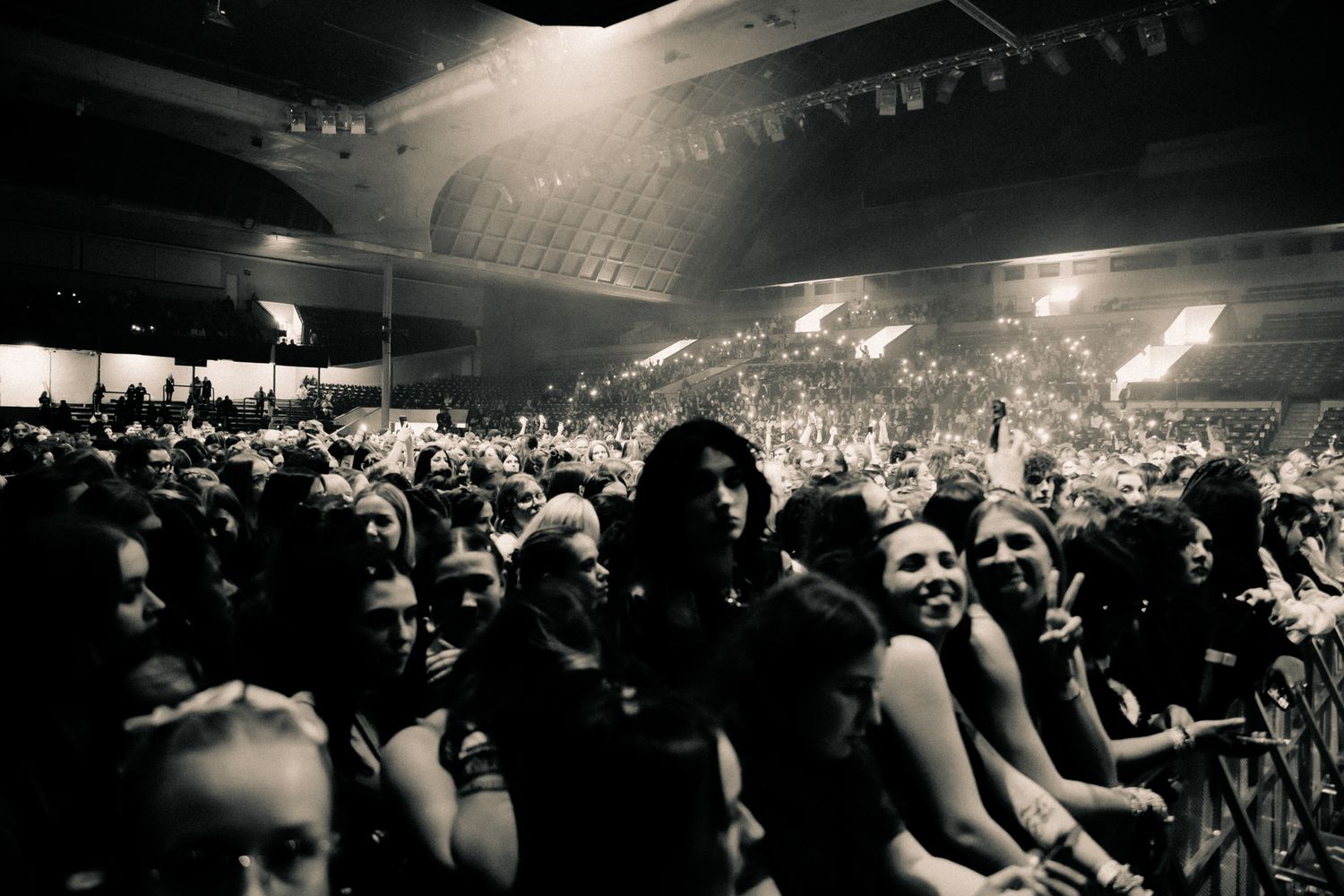 A panoramic black and white photo shows a crowded concert venue with silhouettes of people and stage lighting.