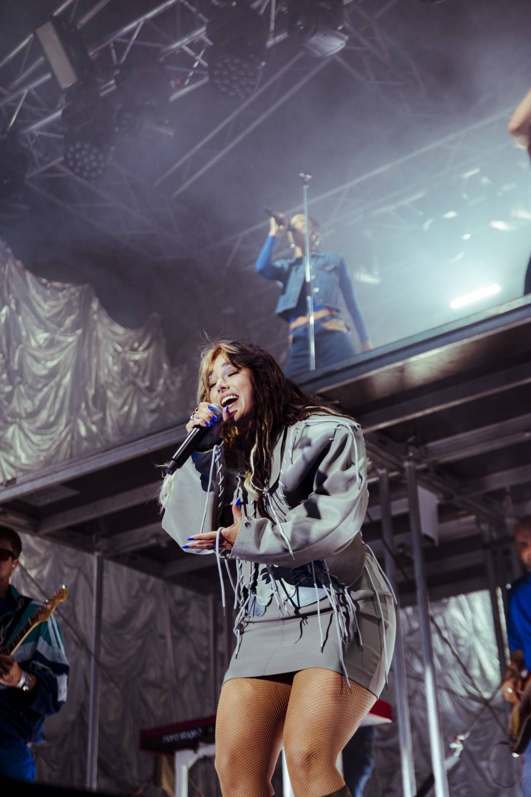 A performer in a gray hoodie sings passionately on stage under dramatic lighting at a concert venue.