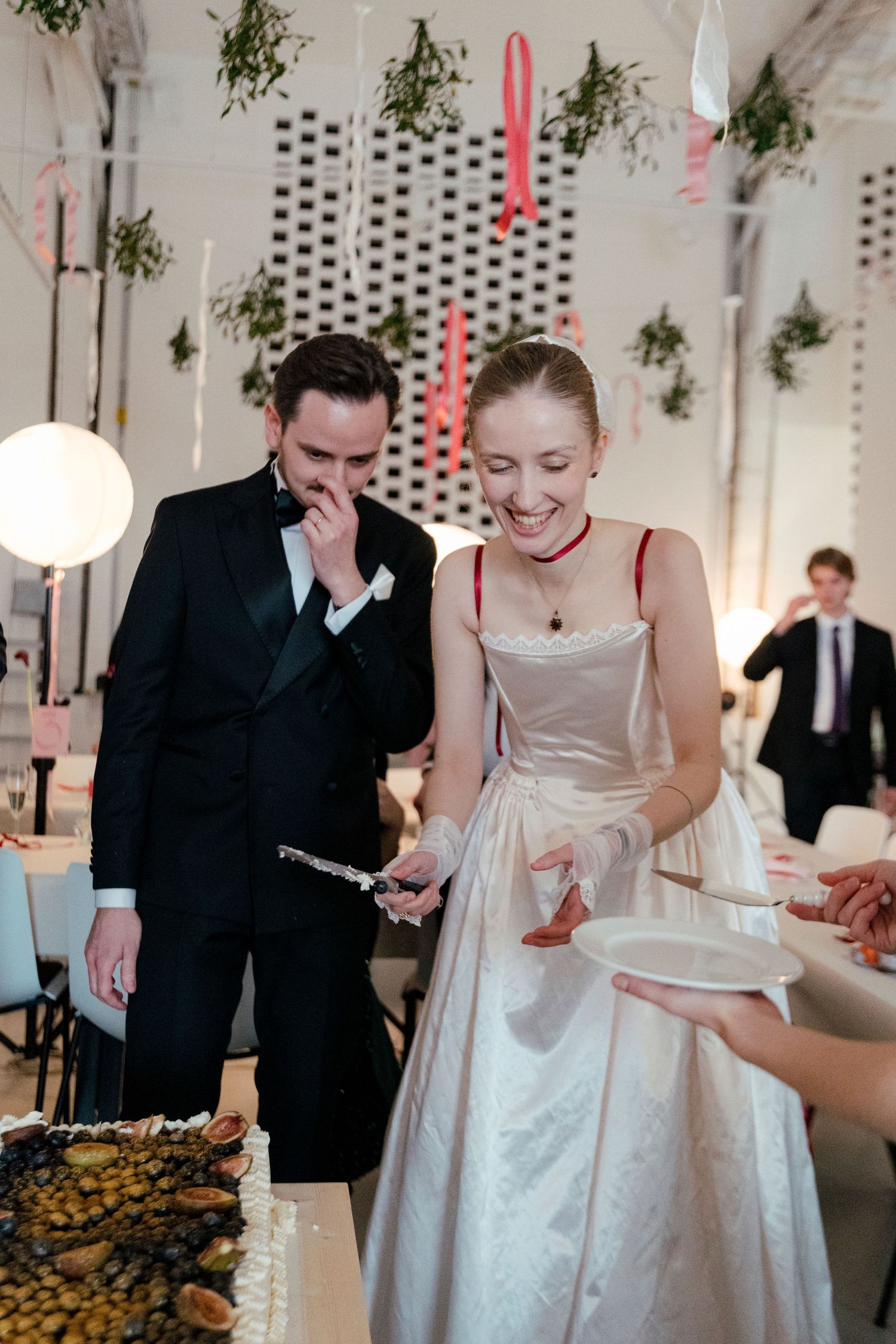 Wedding reception guests gather around a buffet table decorated with greenery and white decor at an elegant indoor venue.