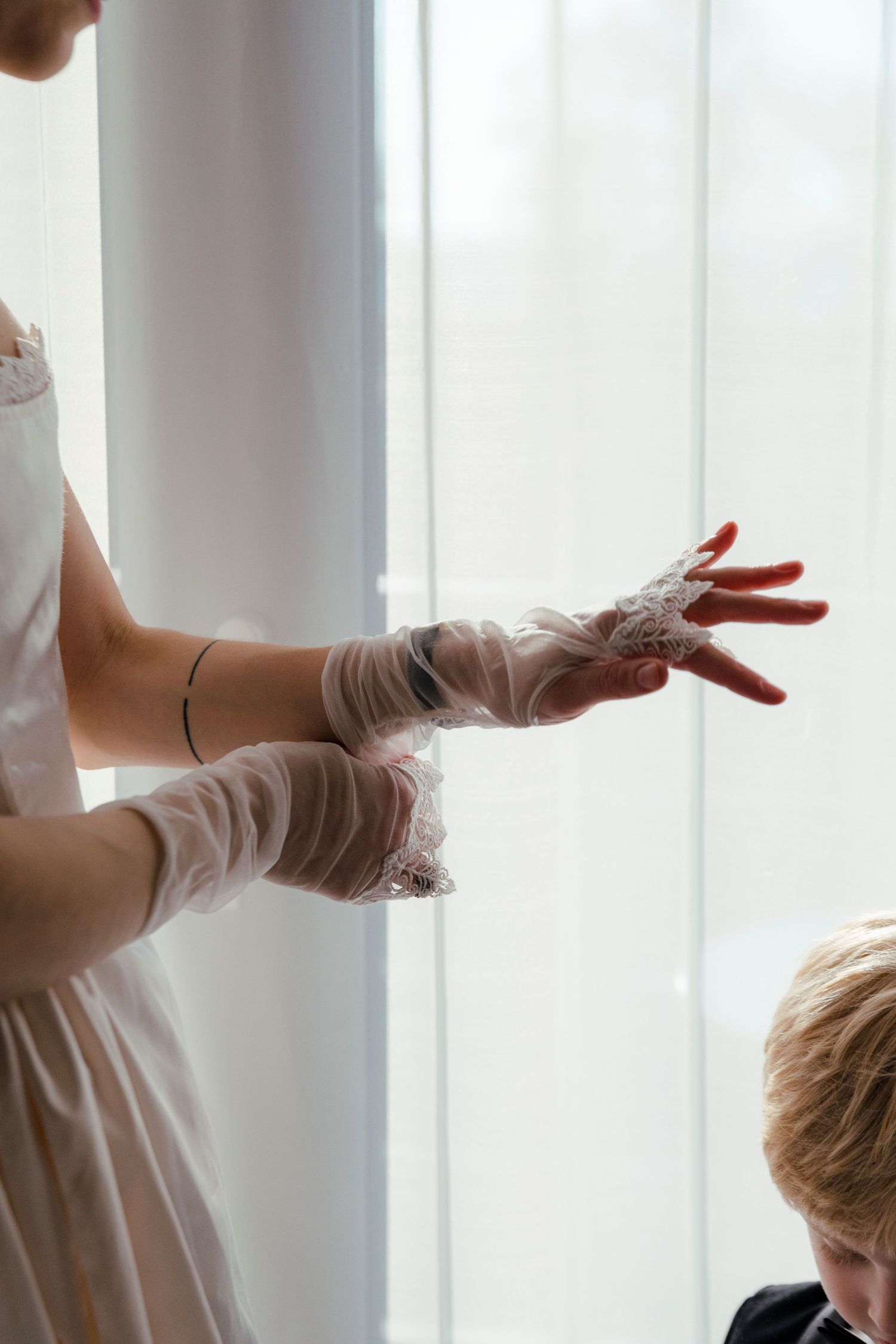 Delicate lace gloves being worn against a bright window background.