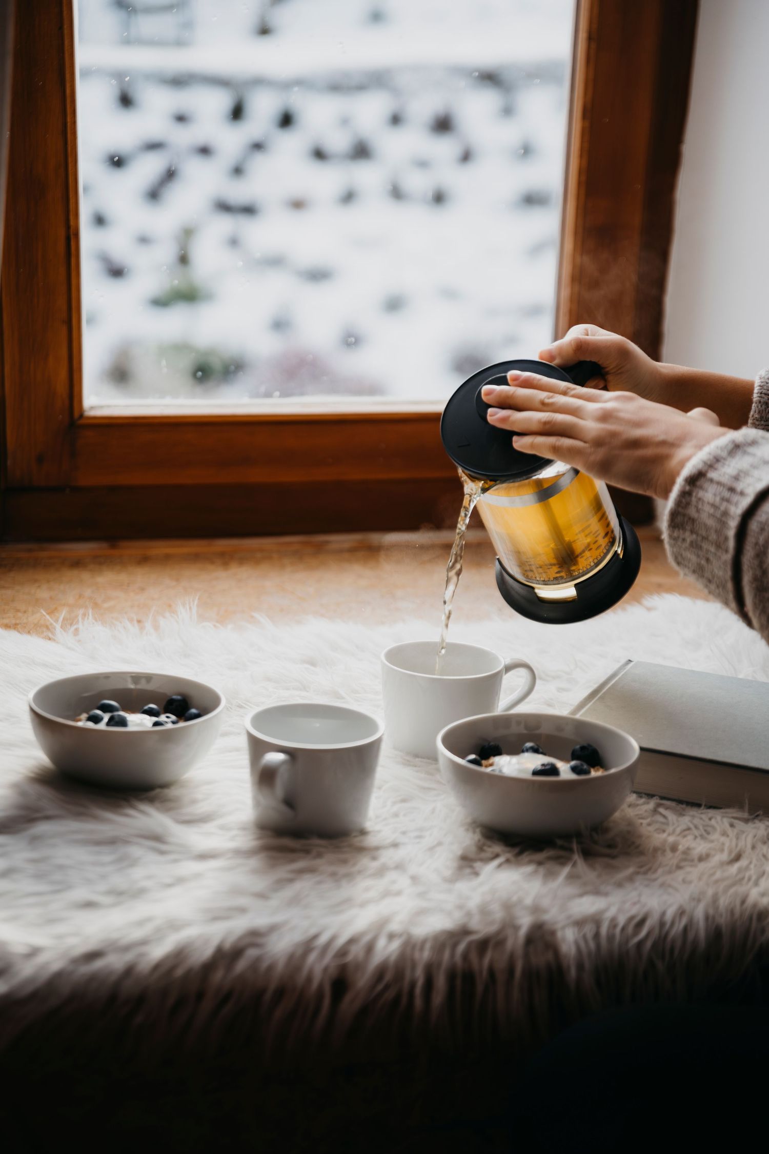 Coffee cups and bowls arranged on windowsill with snowy scene outside.