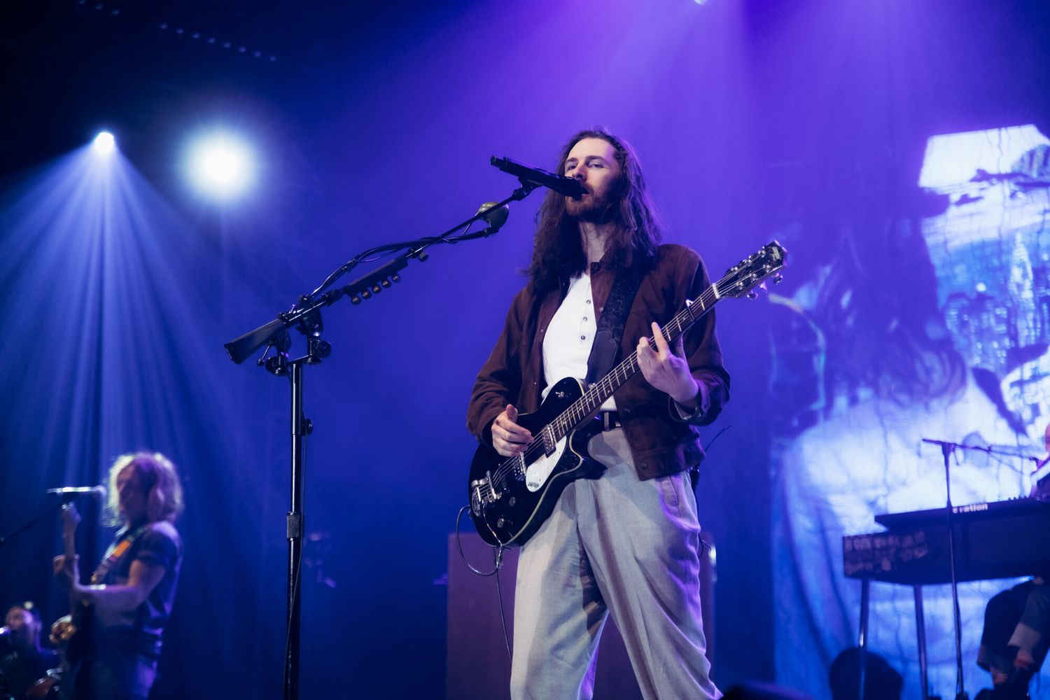 Musicians perform on stage with electric guitars under dramatic blue lighting and fog effects during a live concert.