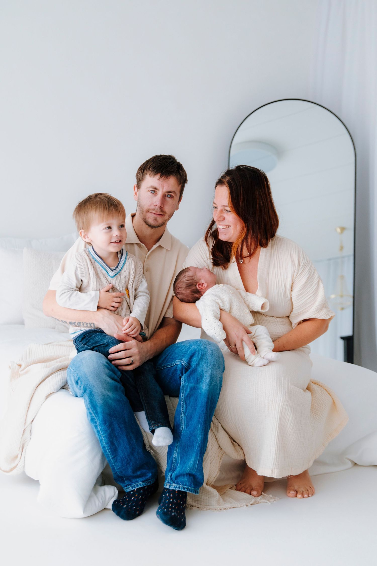 Family relaxing together on white couch in minimalist setting.