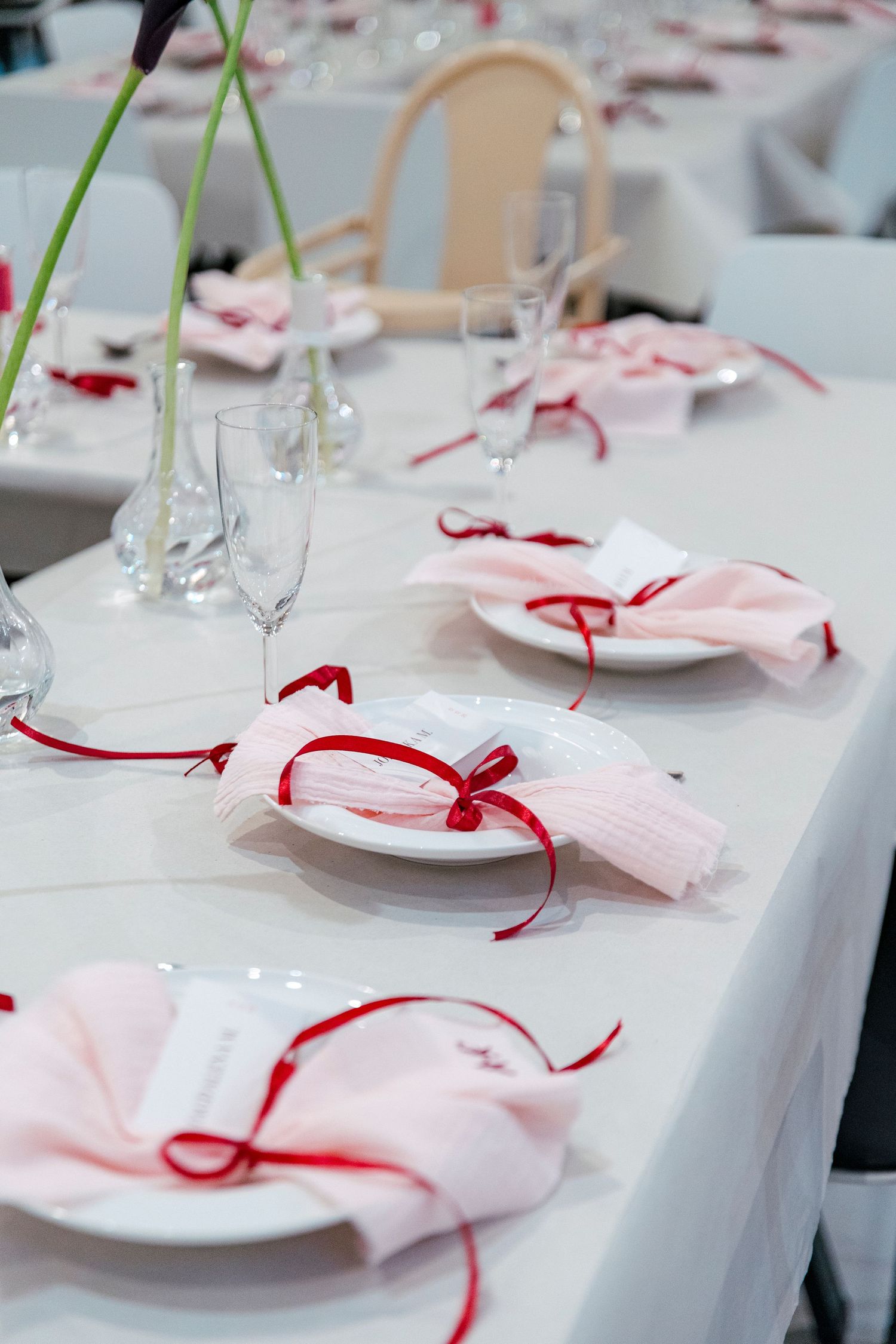Elegant table setting with pink napkins tied with red ribbons on white tablecloth and wine glasses for formal dining.