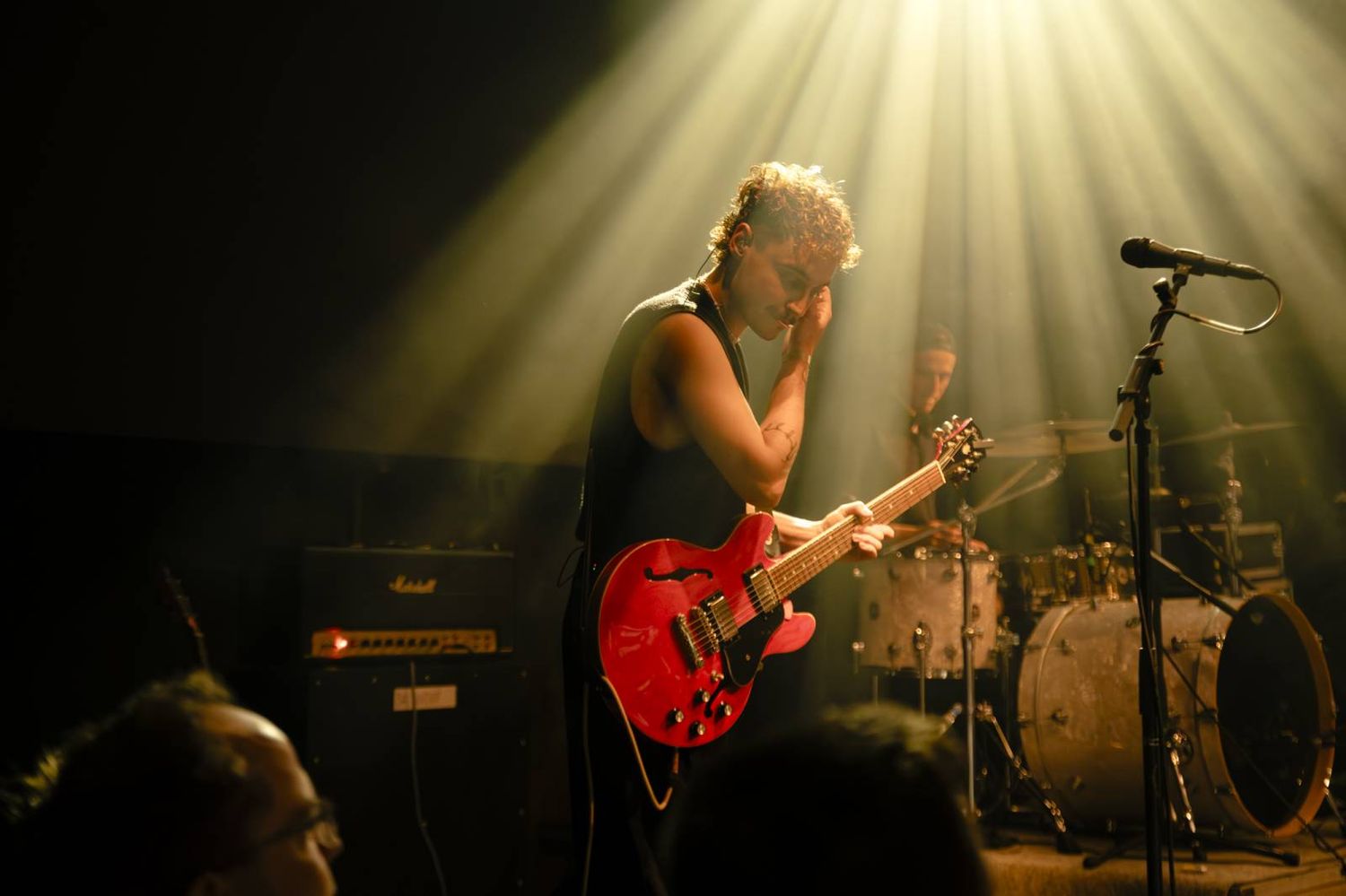 Musicians performing under dramatic yellow spotlight beams in a dark concert venue.