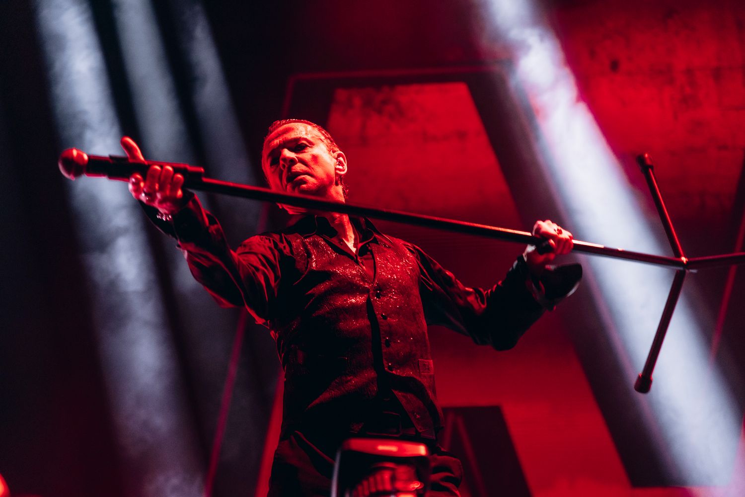 Dramatic concert performance with red lighting and spotlights illuminating a performer on stage.