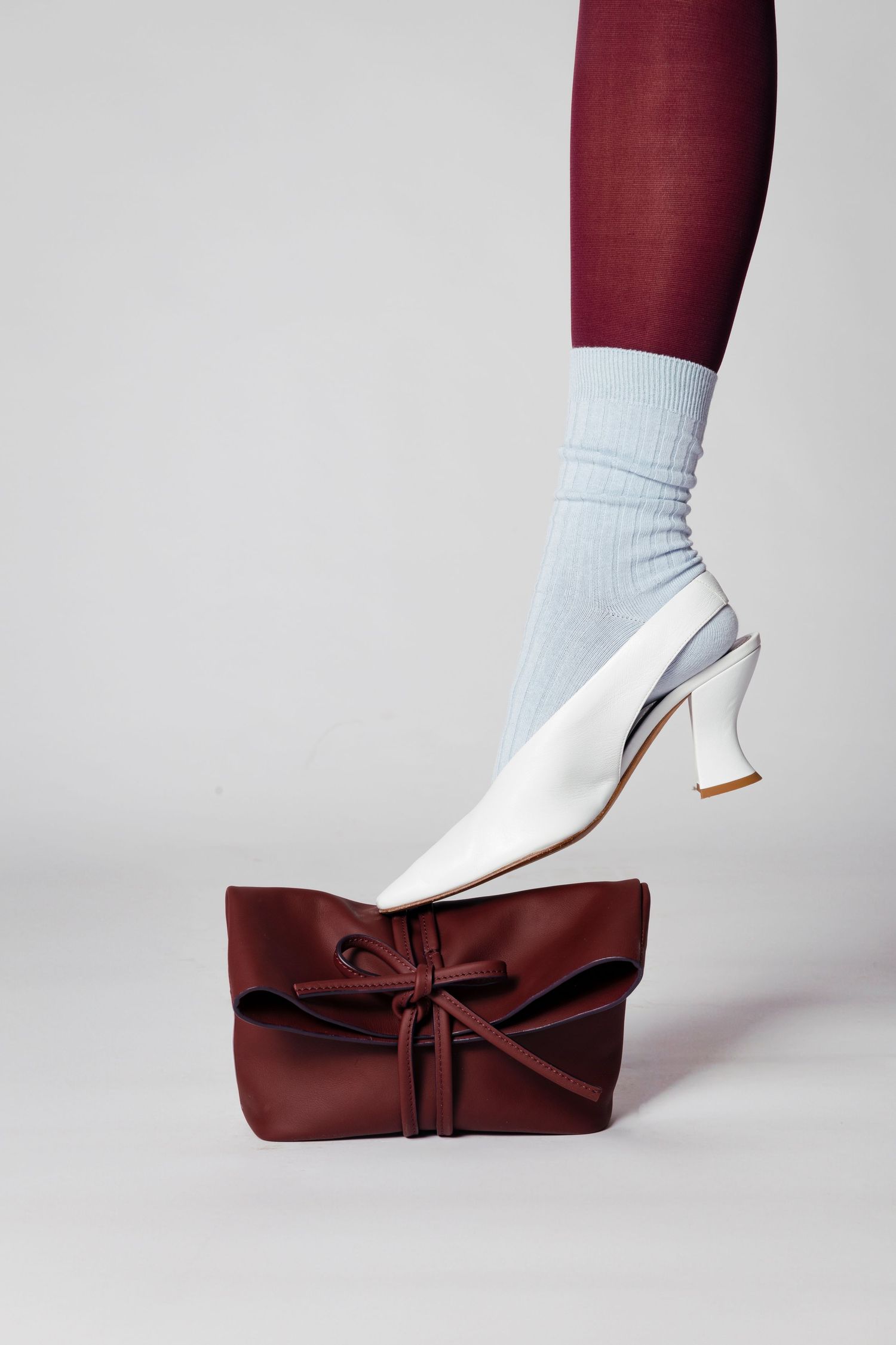 White heel shoe with burgundy bow accessory against grey background.