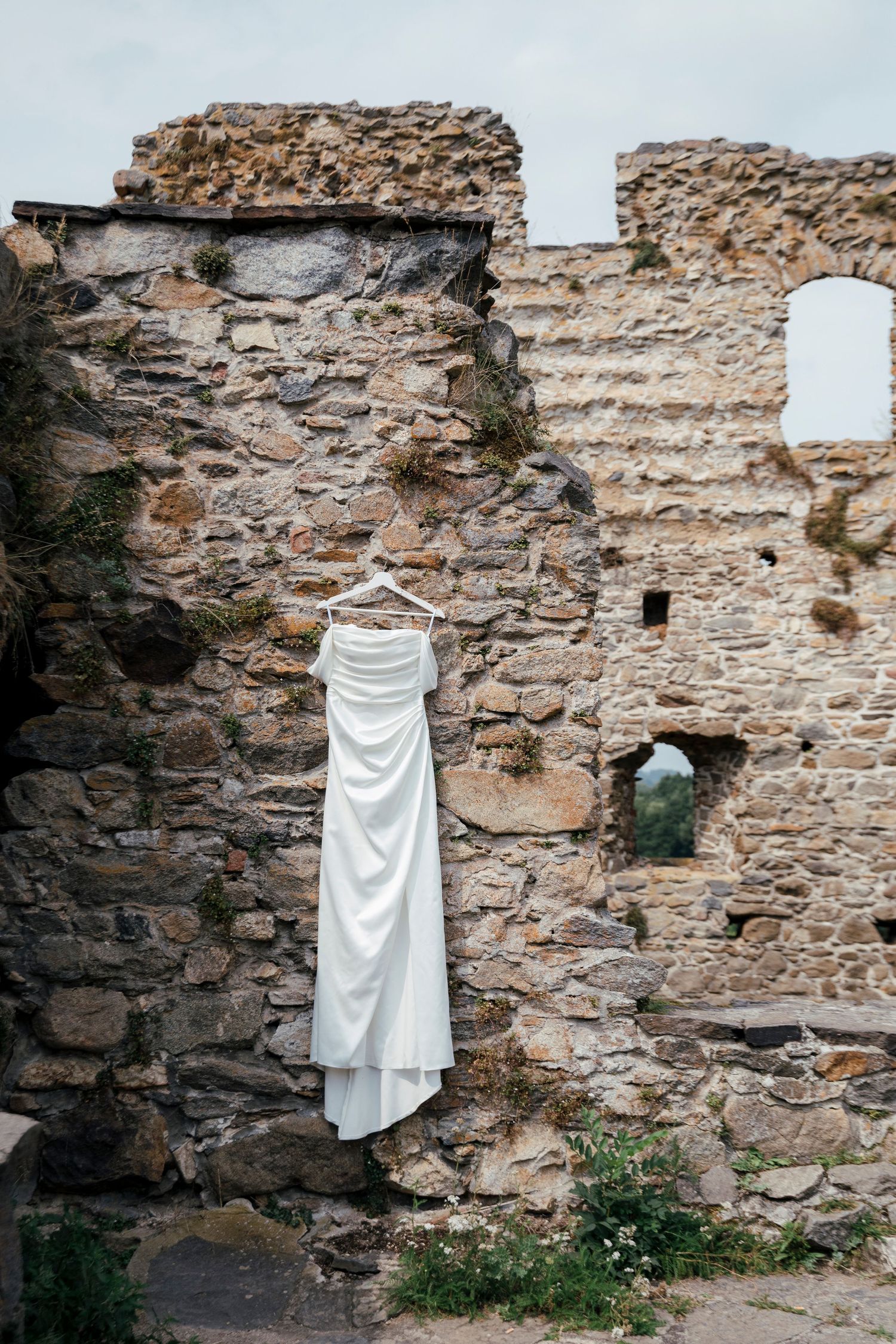 White wedding dress hanging against rustic stone wall backdrop.