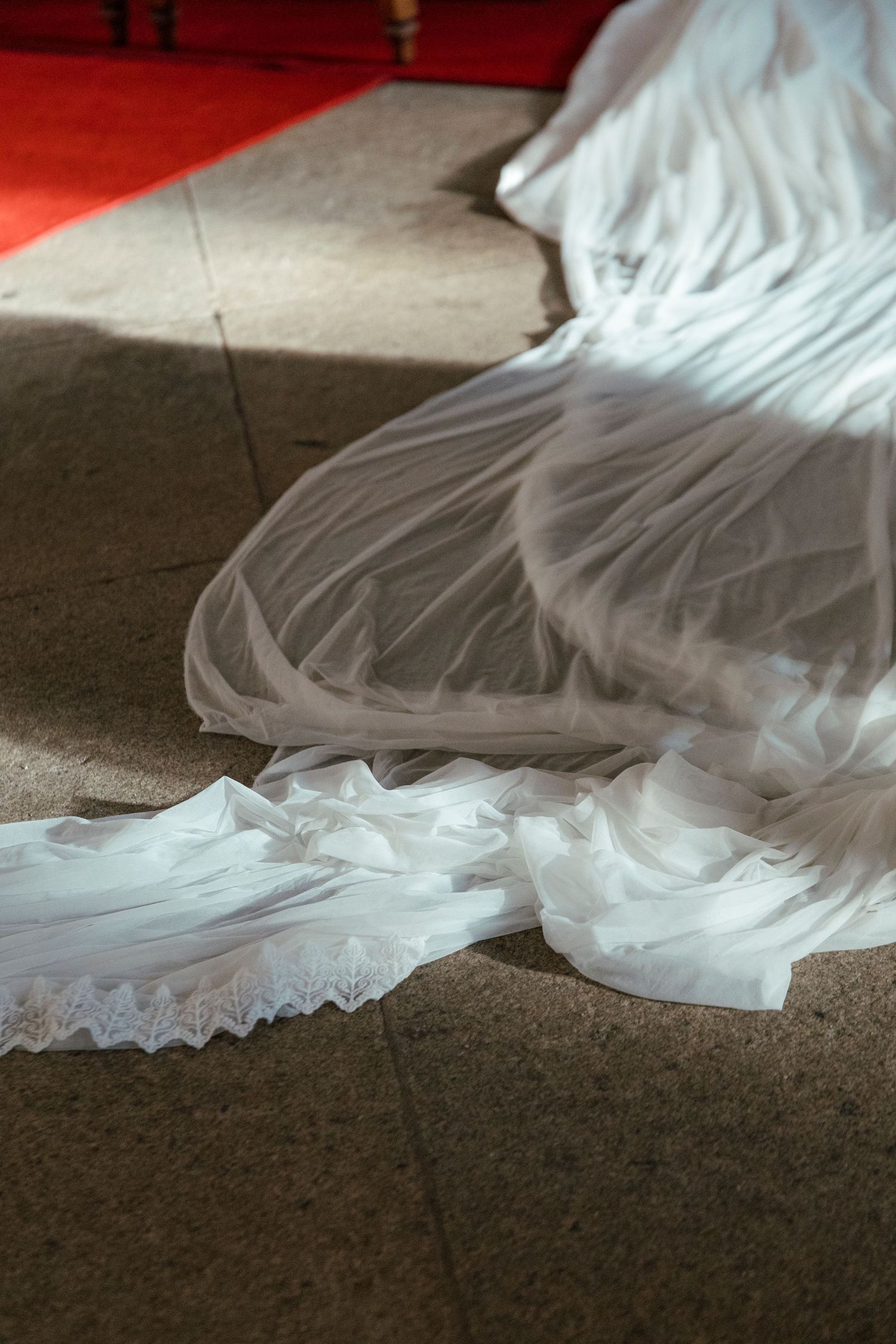 White wedding dress train with delicate lace details trails along a dark floor in dramatic lighting.