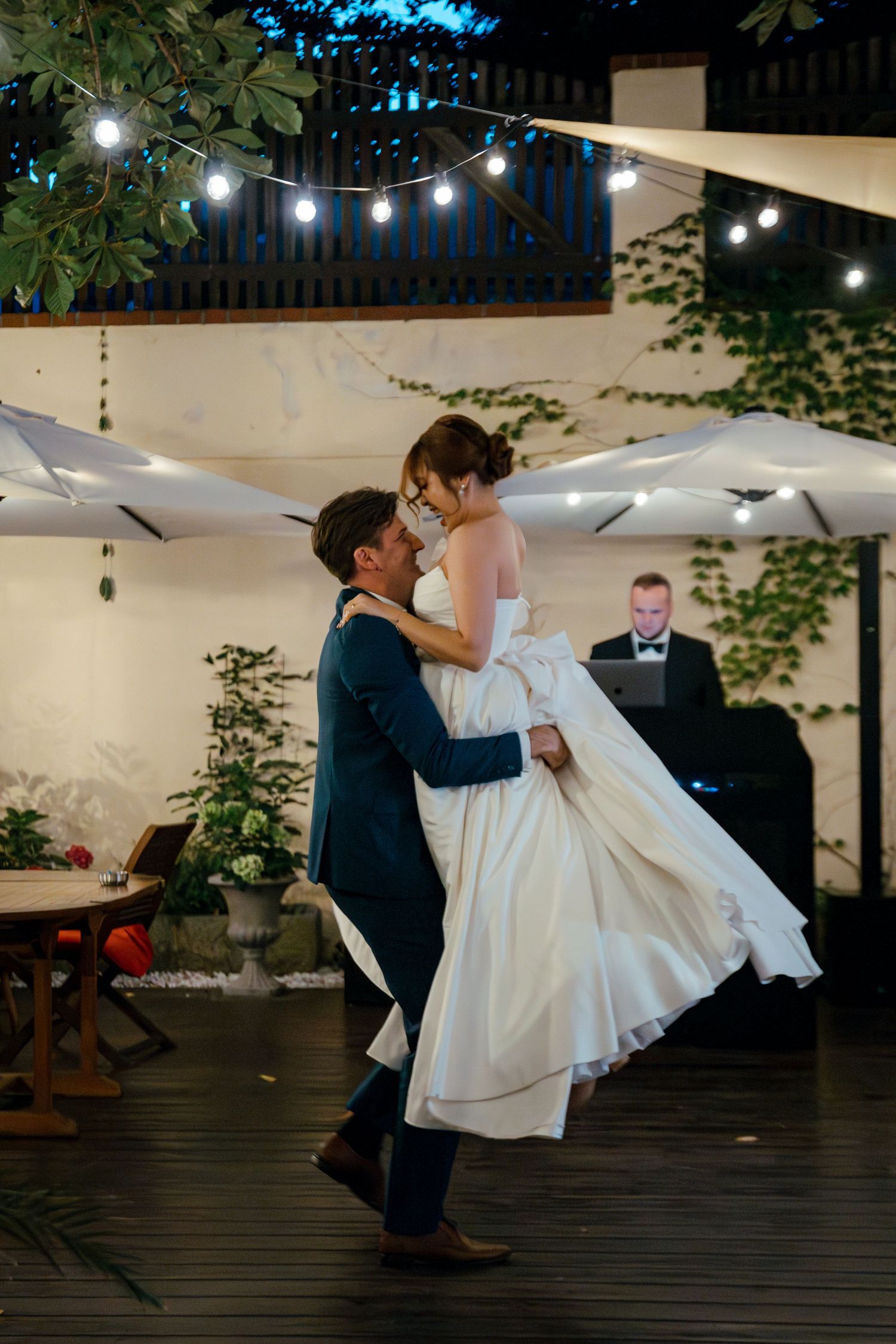 Romantic dance sequence of newlyweds on an outdoor deck with string lights overhead.