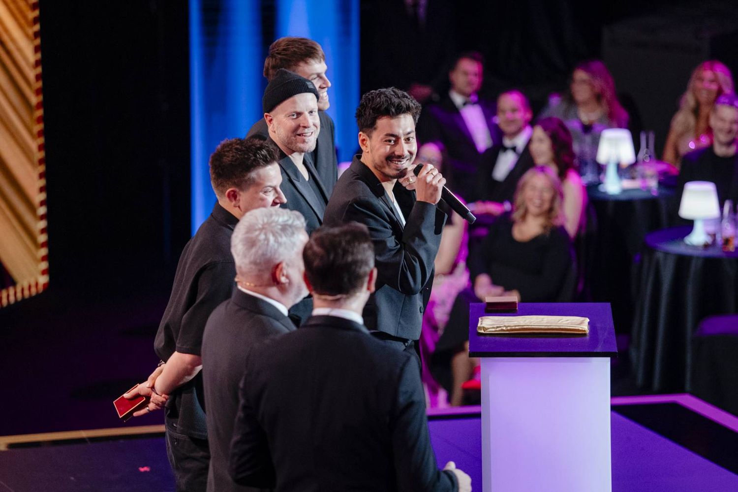 A crowd gathers at an indoor event venue with purple mood lighting and stage setup.