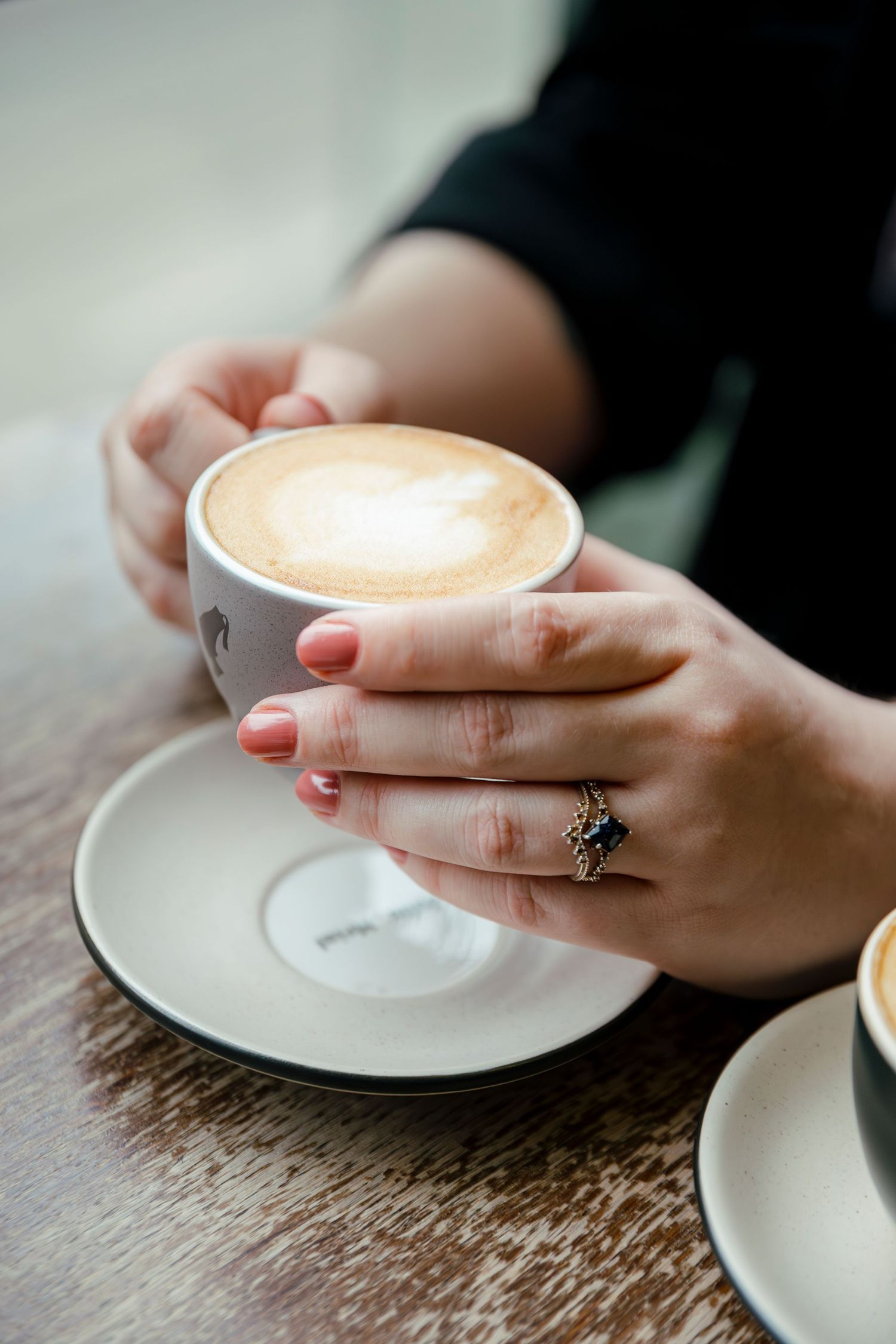 Close-up of hands holding a latte cup with engagement ring visible.