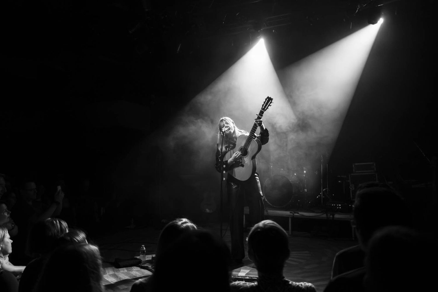 Black and white photo of performer on stage illuminated by dramatic overhead spotlights during concert.