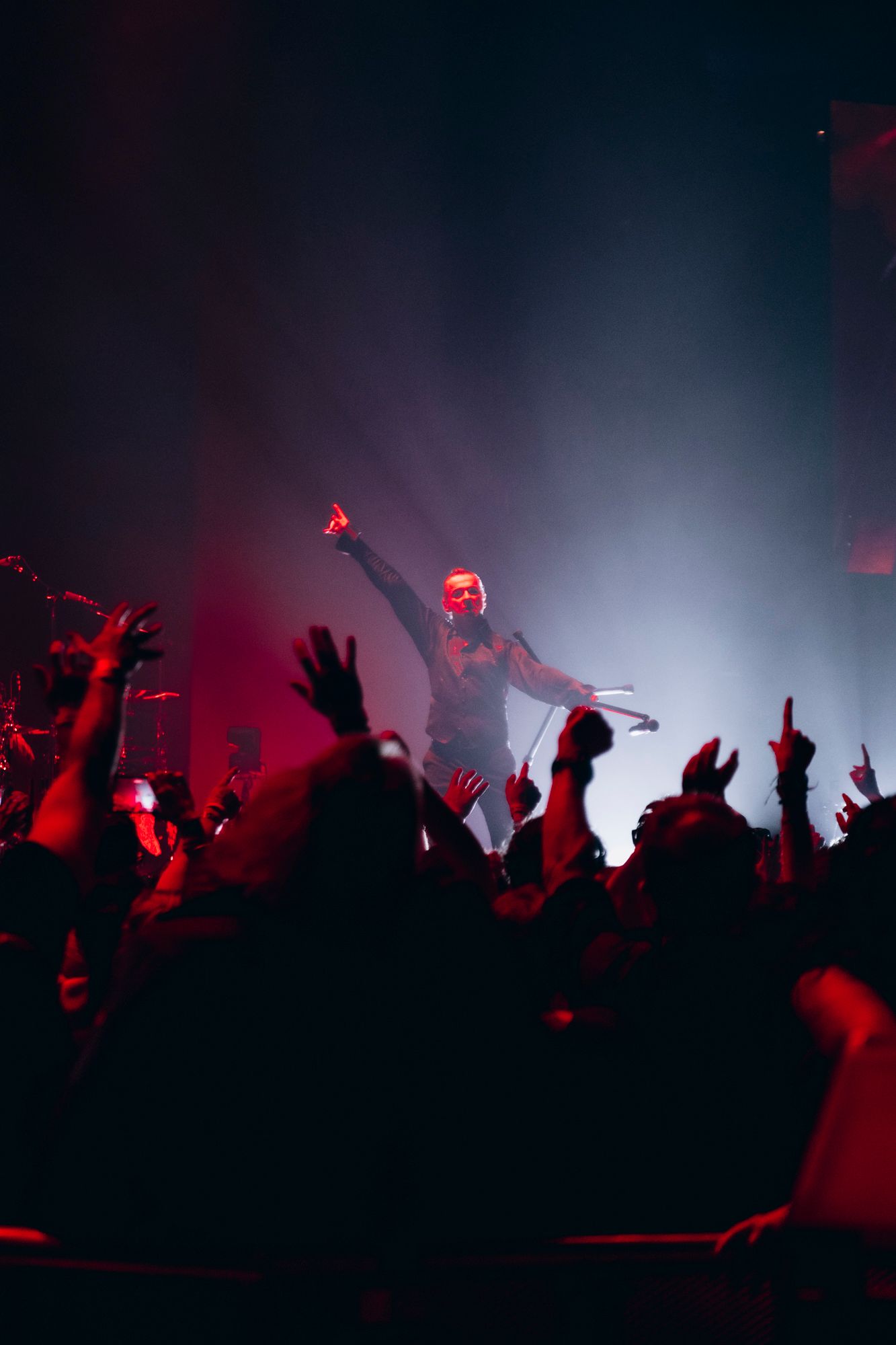 Silhouetted crowd with raised hands at a concert illuminated by dramatic red and white lighting effects.