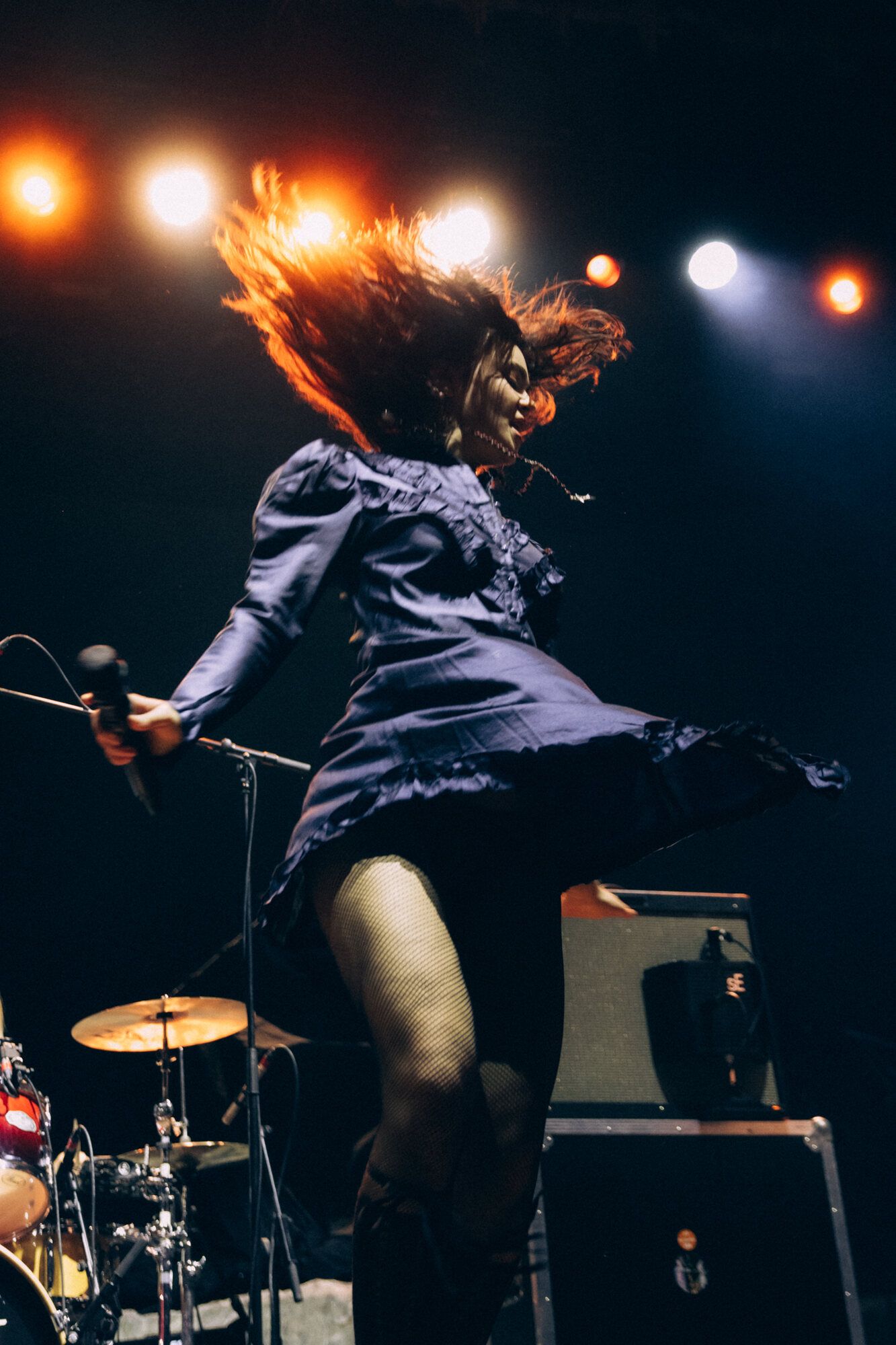 Dynamic concert performance captured in motion with dramatic lighting showing energetic musician on dark stage with drums.