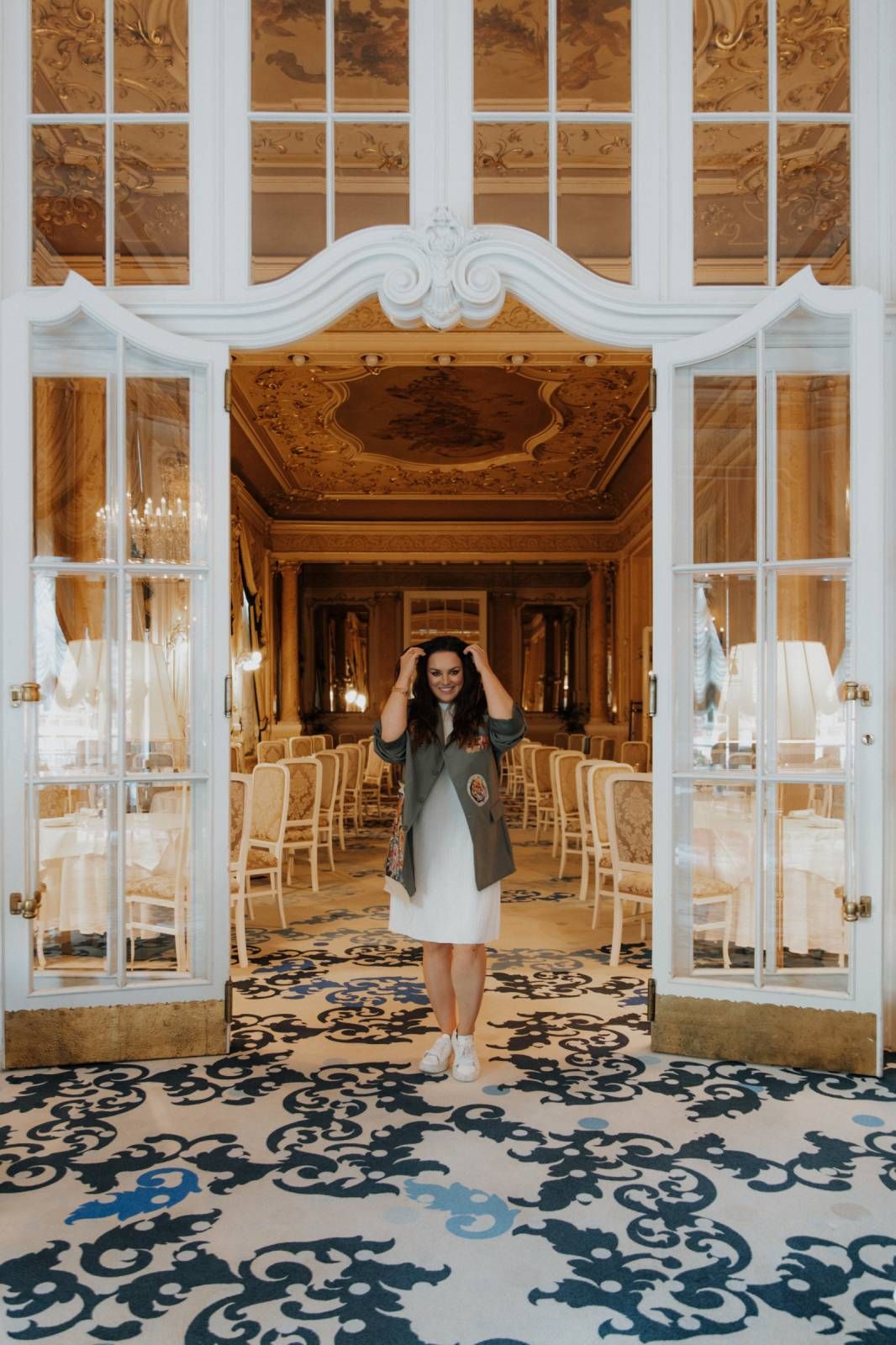 Elegant doorway entrance to ornate ballroom with white French doors and intricate black patterned carpet at luxury venue.