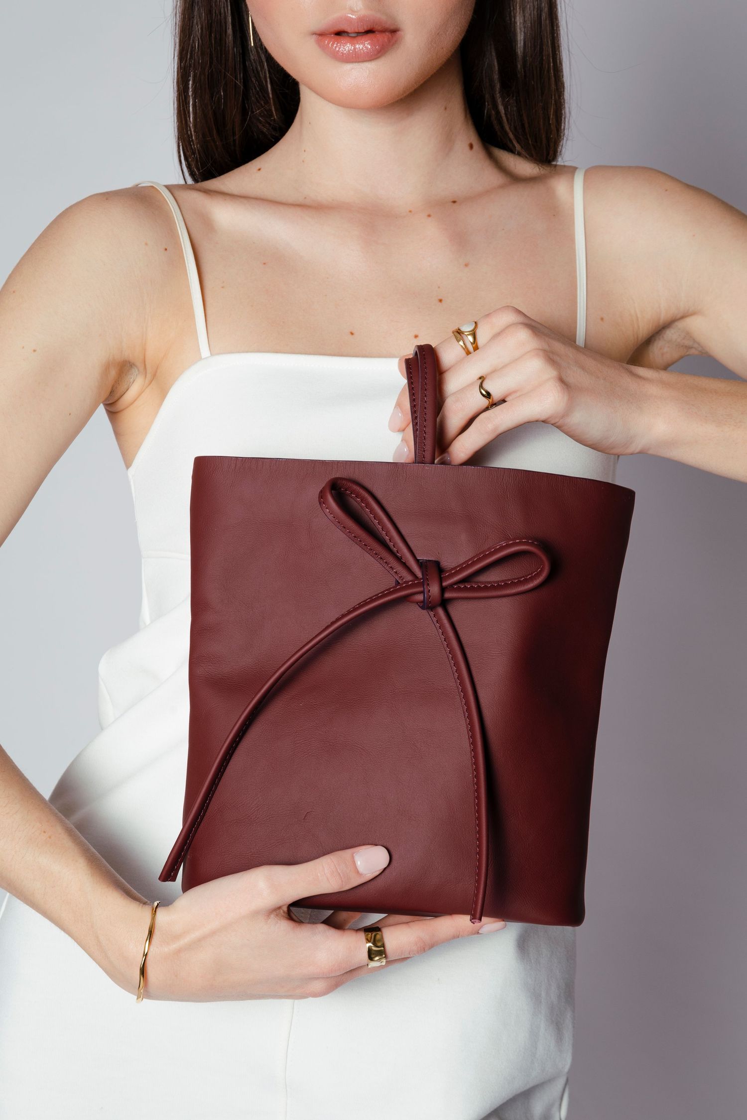 Burgundy leather clutch with bow detail displayed against white top.