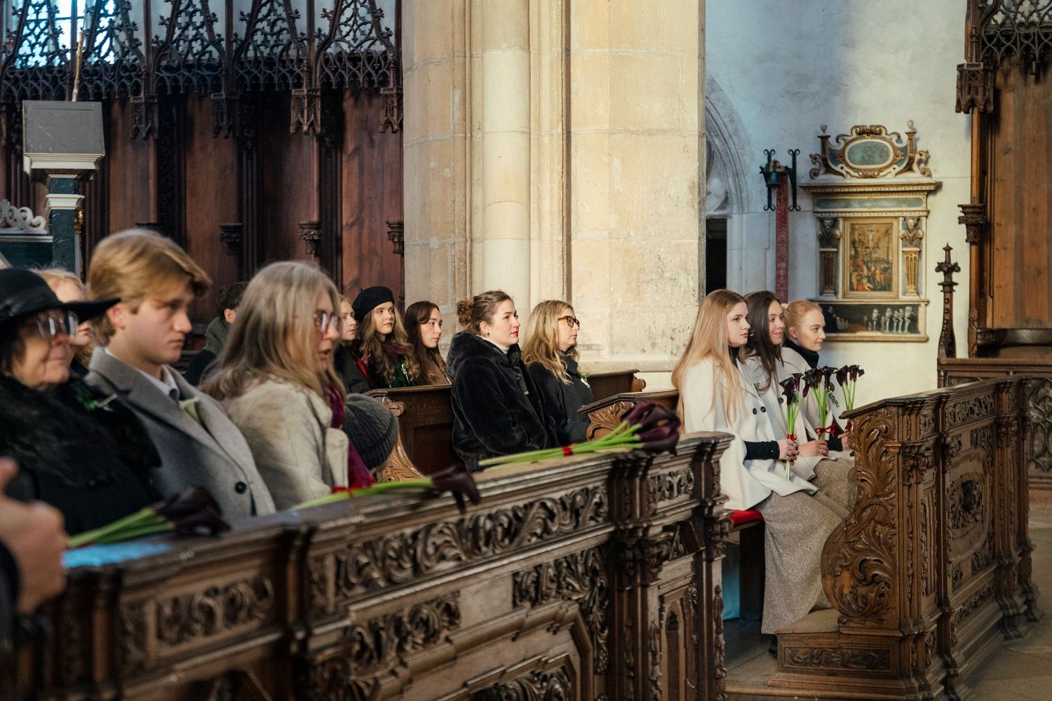 Wedding guests seated in wooden church pews during ceremony in historic cathedral.
