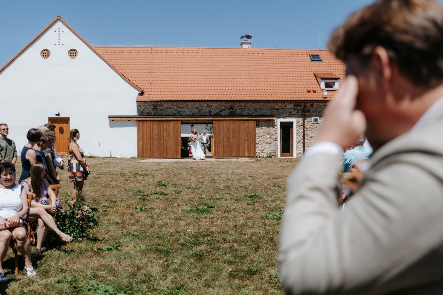 Wedding photographer captures guests watching ceremony at rustic barn venue.