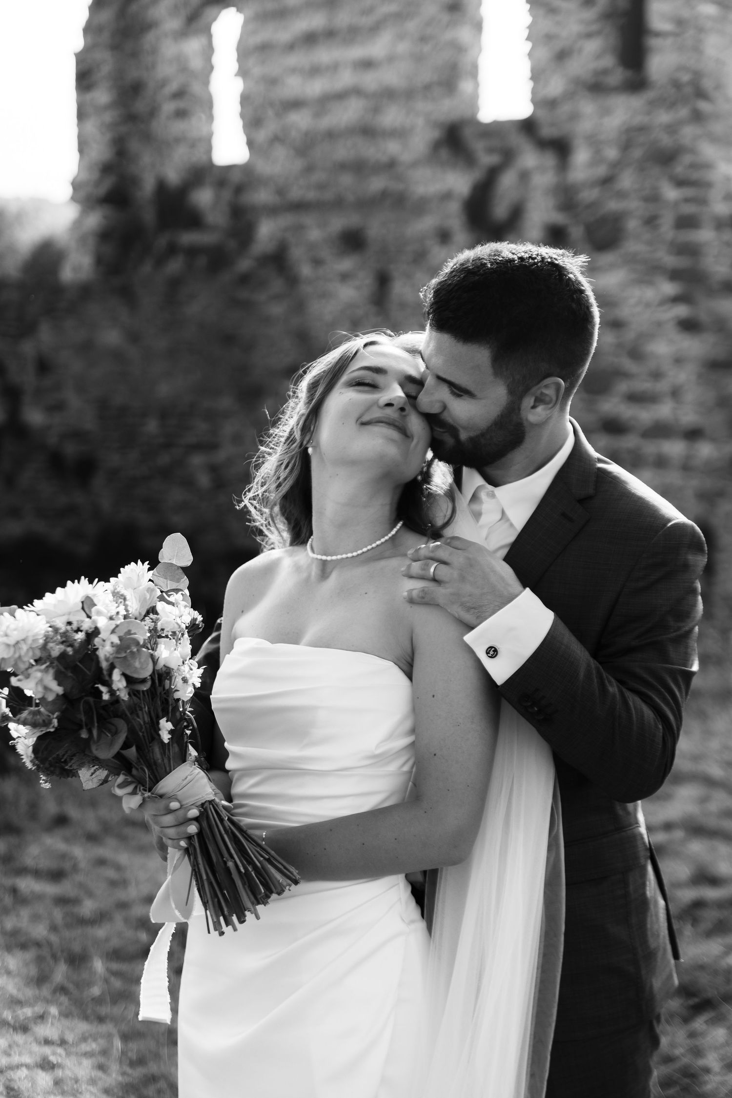 Romantic black and white wedding photo series showing intimate moments between newlyweds against stone wall backdrop.