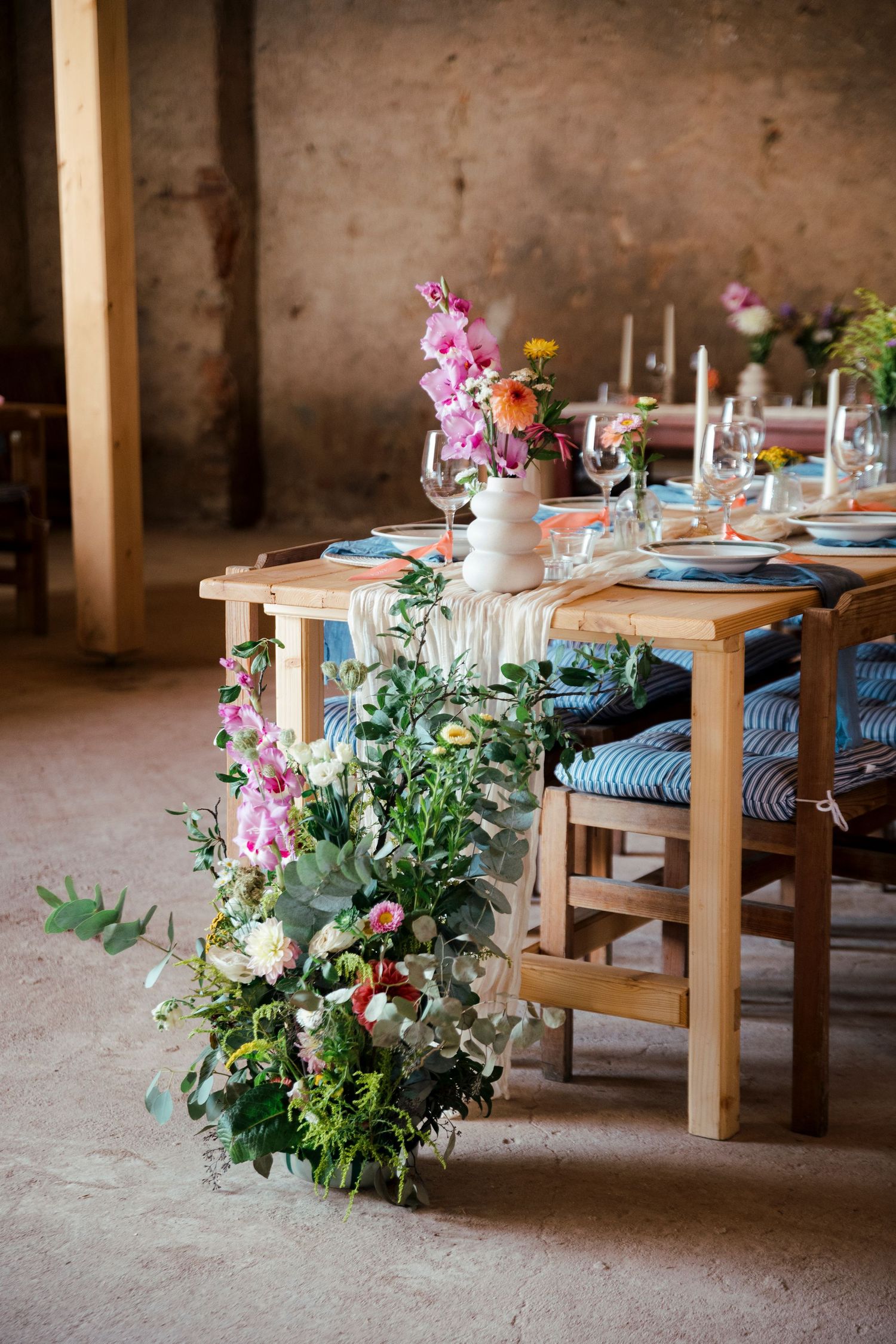 Rustic wedding reception tables decorated with pink floral arrangements and blue cushioned chairs.