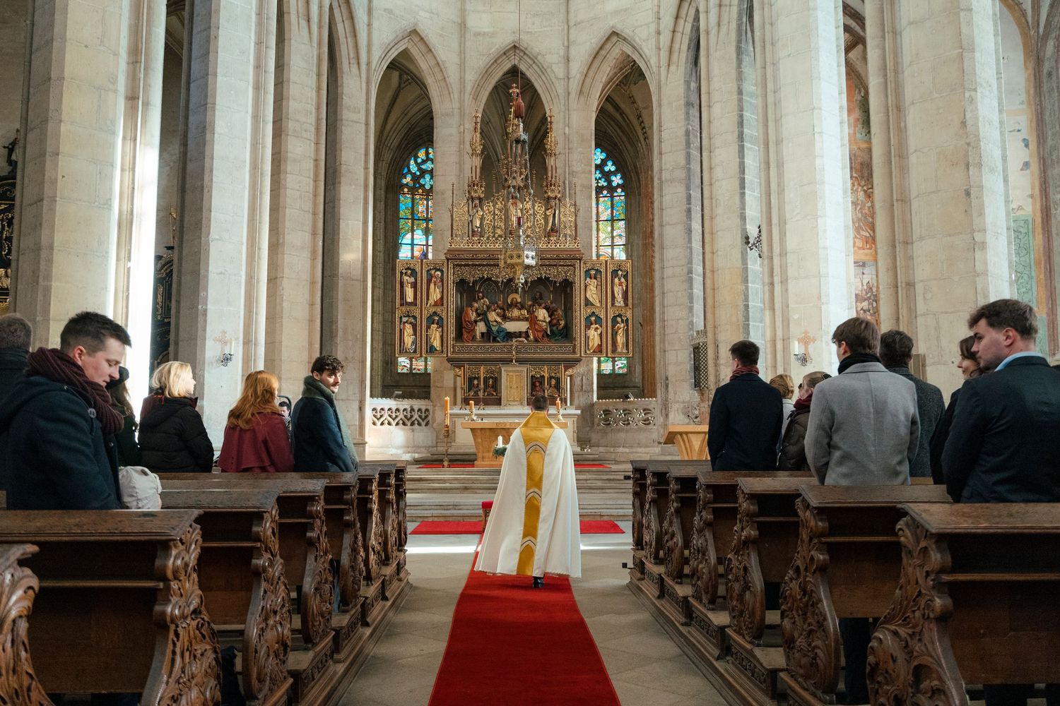Church aisle with wooden pews and red carpet leading to an ornate altar.