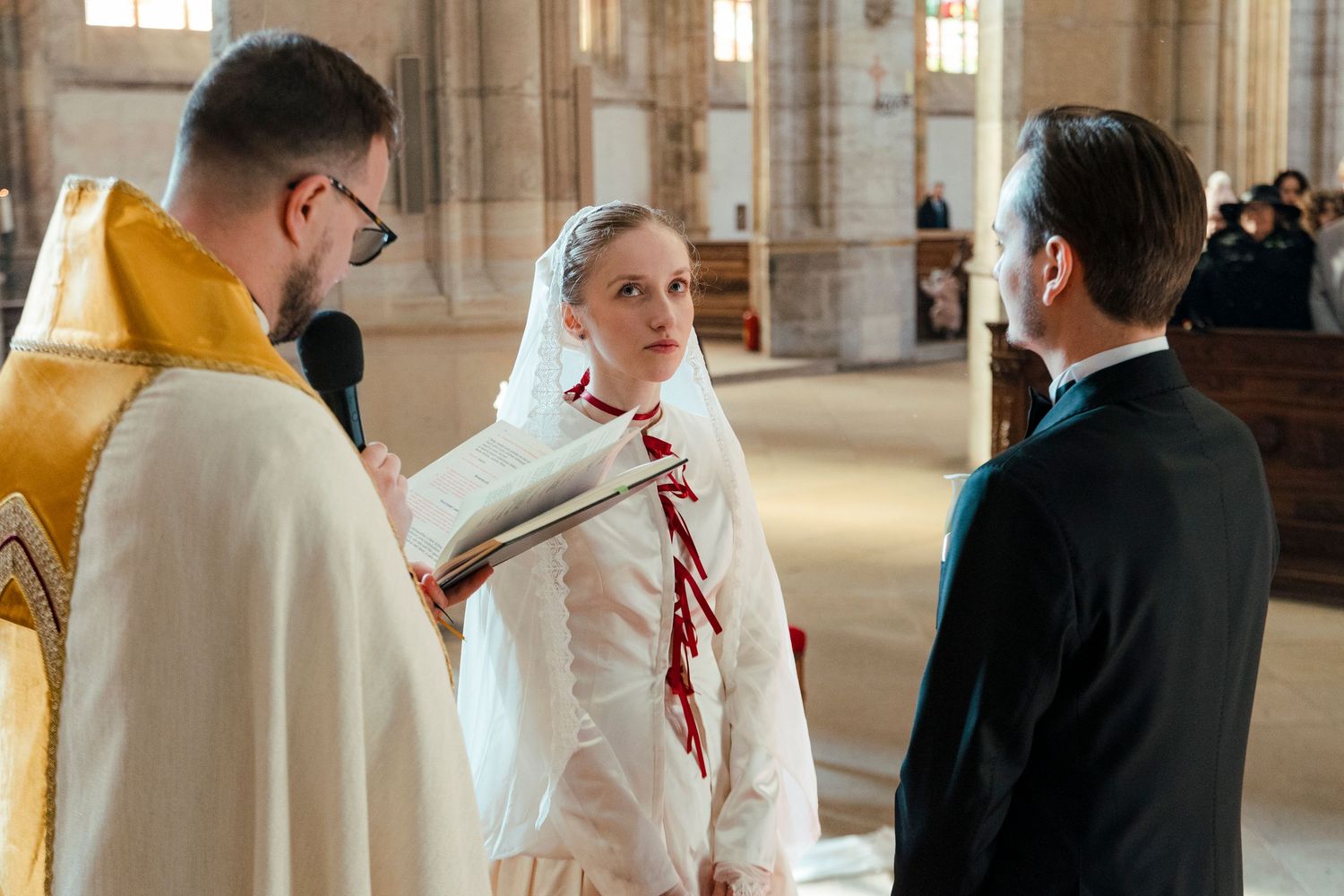 Wedding party members interact in an elegant church interior with tall windows.