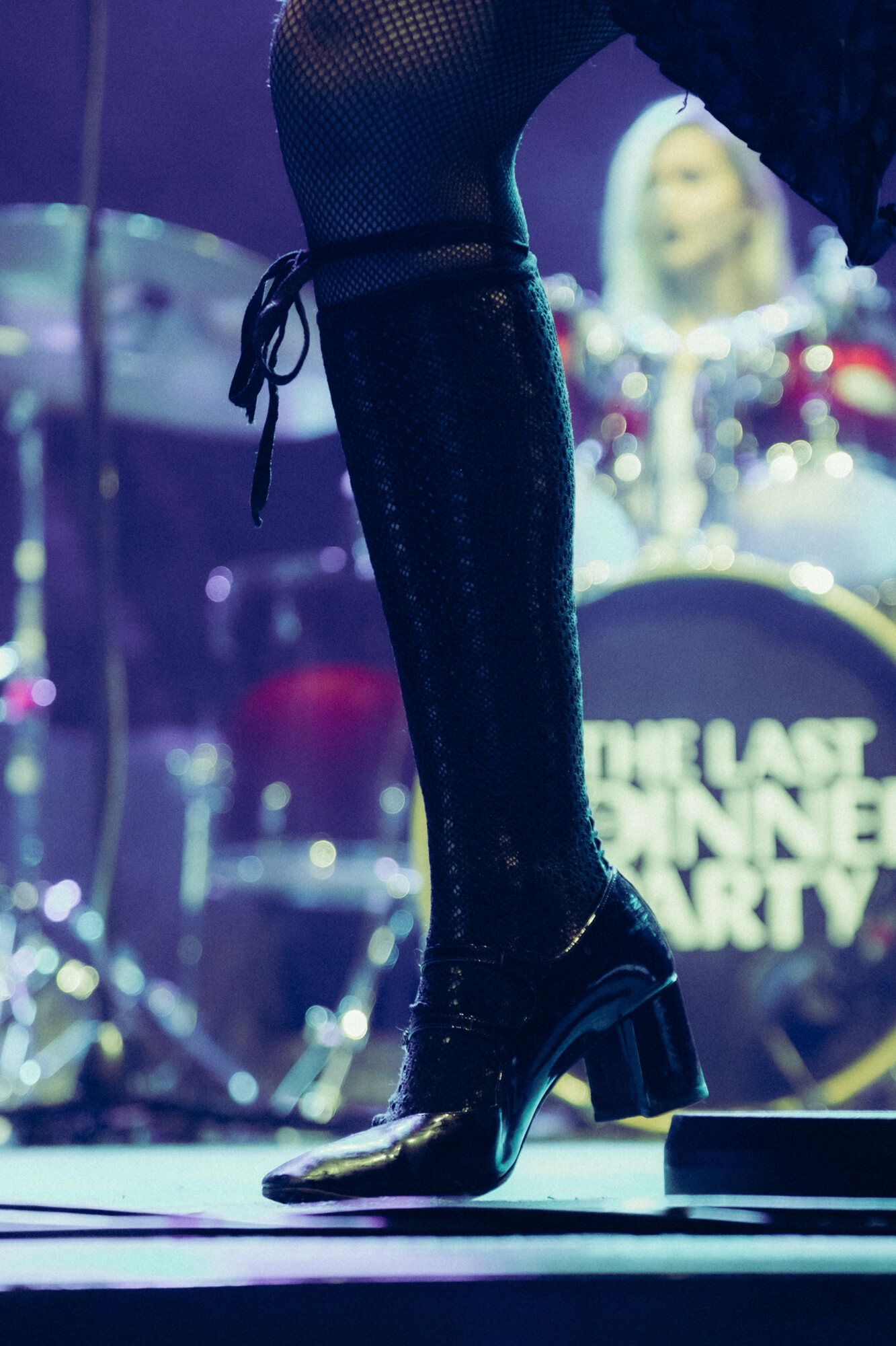 Close-up shots of black high heeled boots on stage with blurred colorful lights in the background.