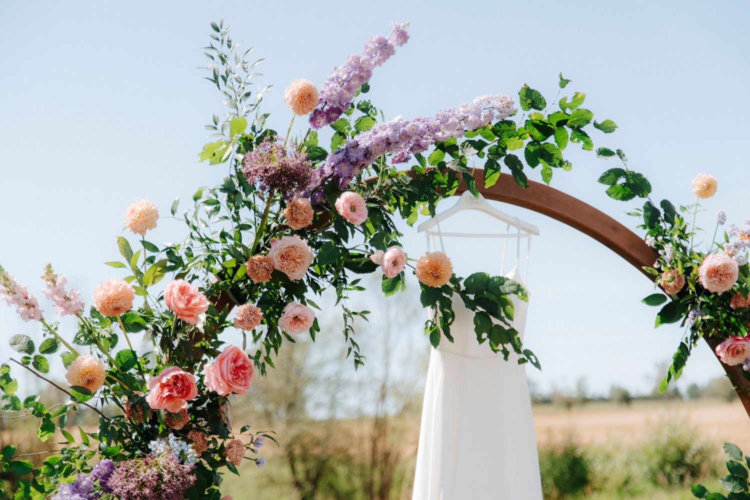 Wedding arch decorated with lush pink and purple flowers against a natural outdoor setting.