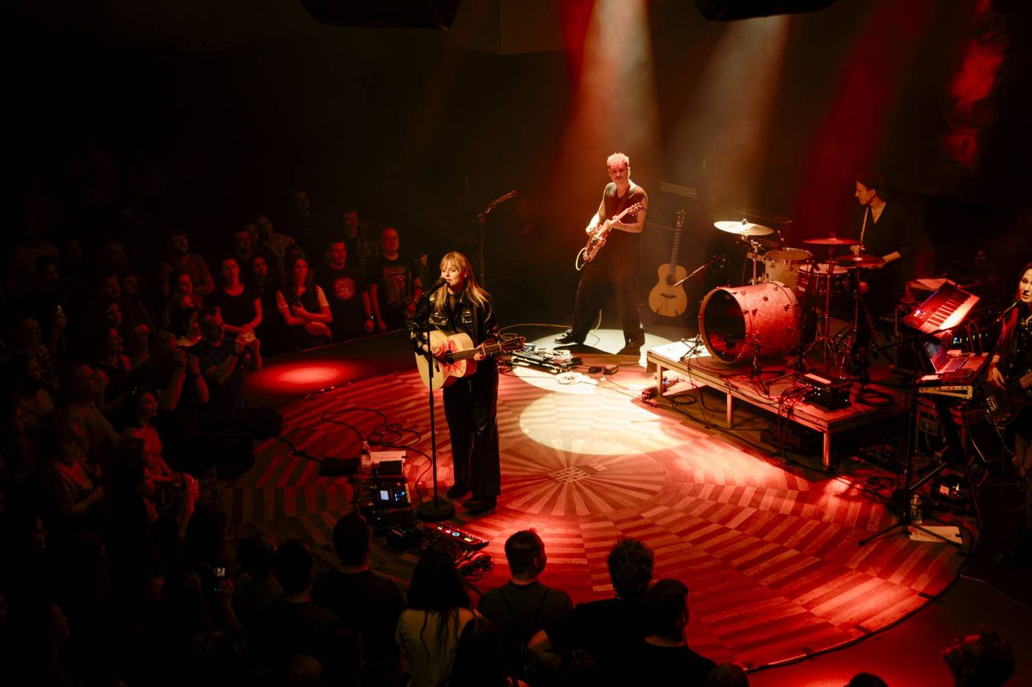 Concert venue with red stage lighting and circular floor pattern surrounded by audience members.