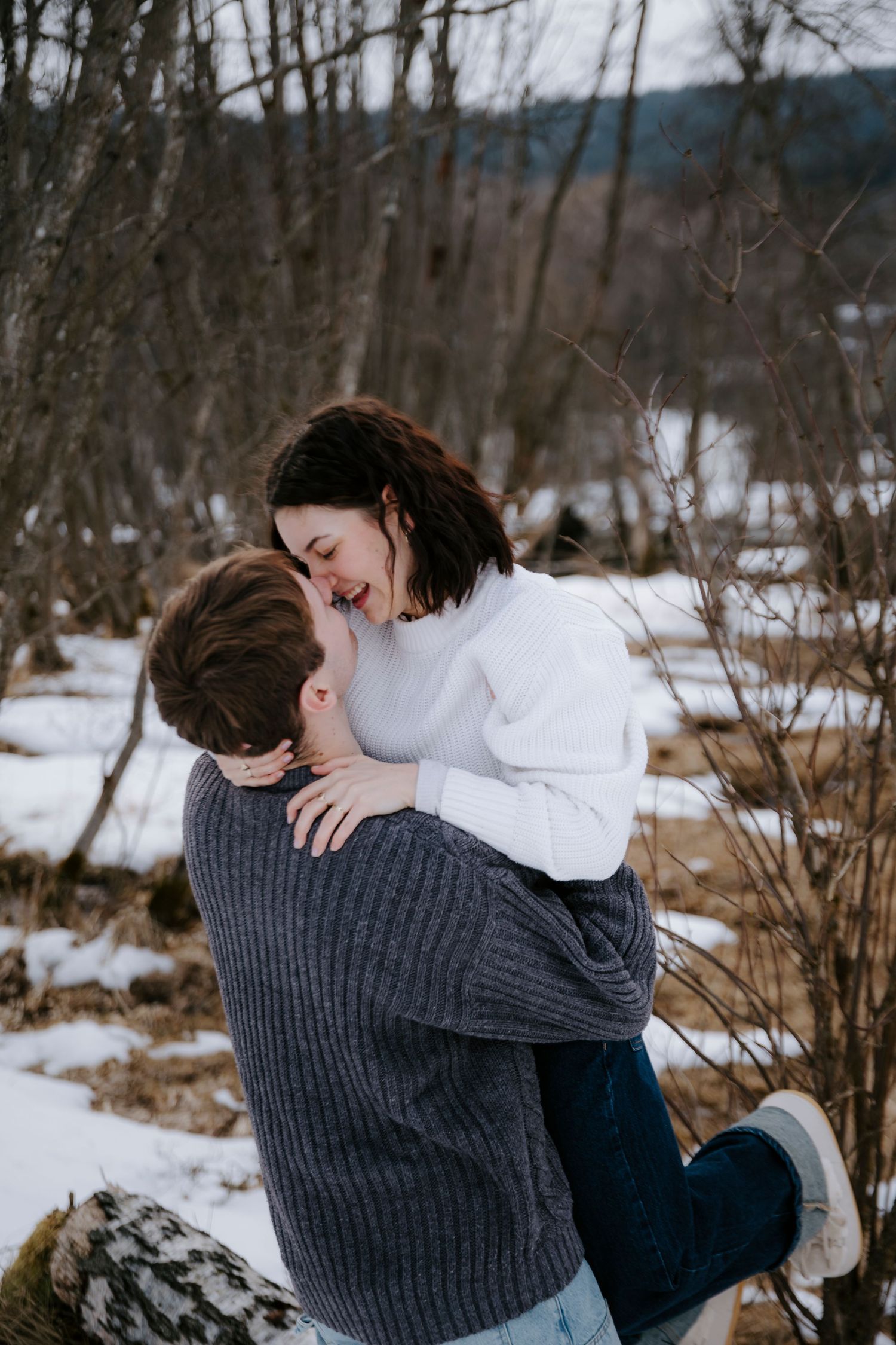 Couple sharing an intimate embrace in a snowy winter forest setting.