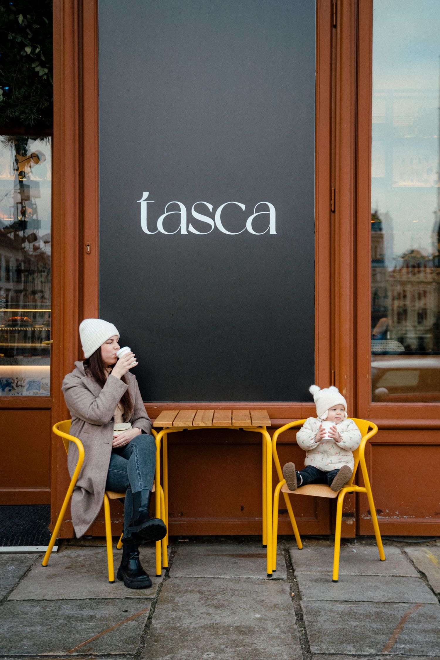 Parent and child sitting at yellow chairs outside Tasca cafe.