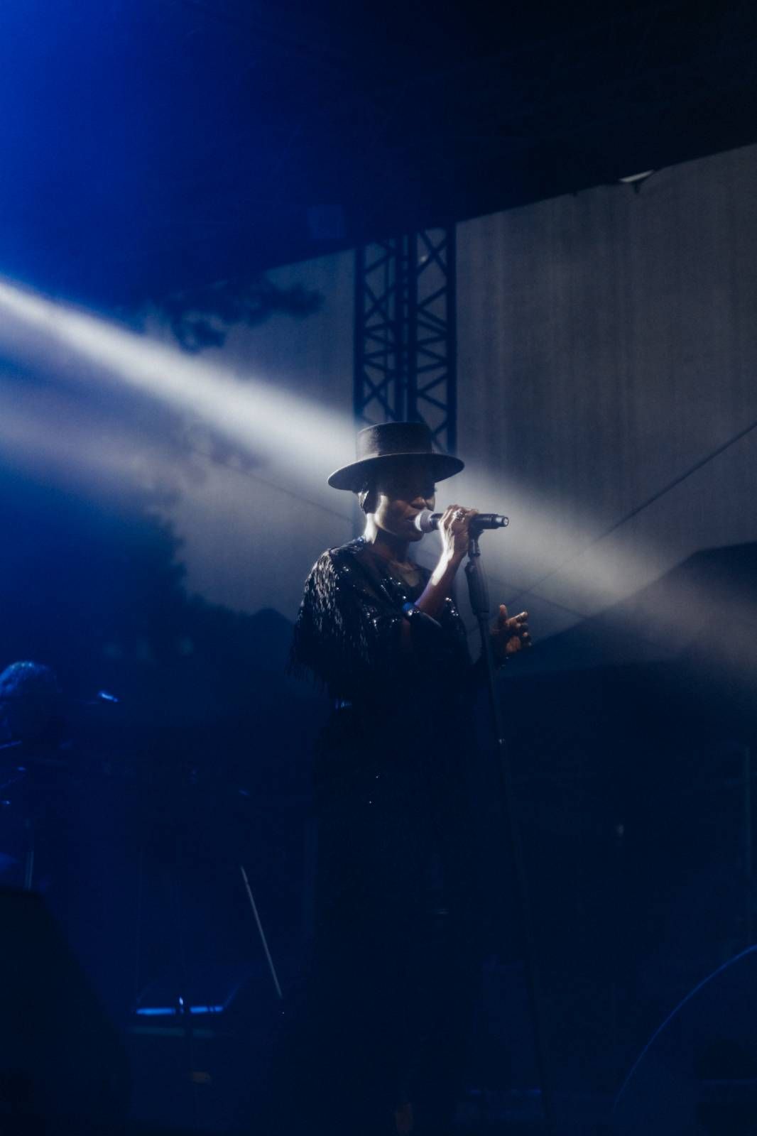 A silhouetted performer sings on stage with dramatic blue lighting and smoke effects creating an atmospheric concert scene.